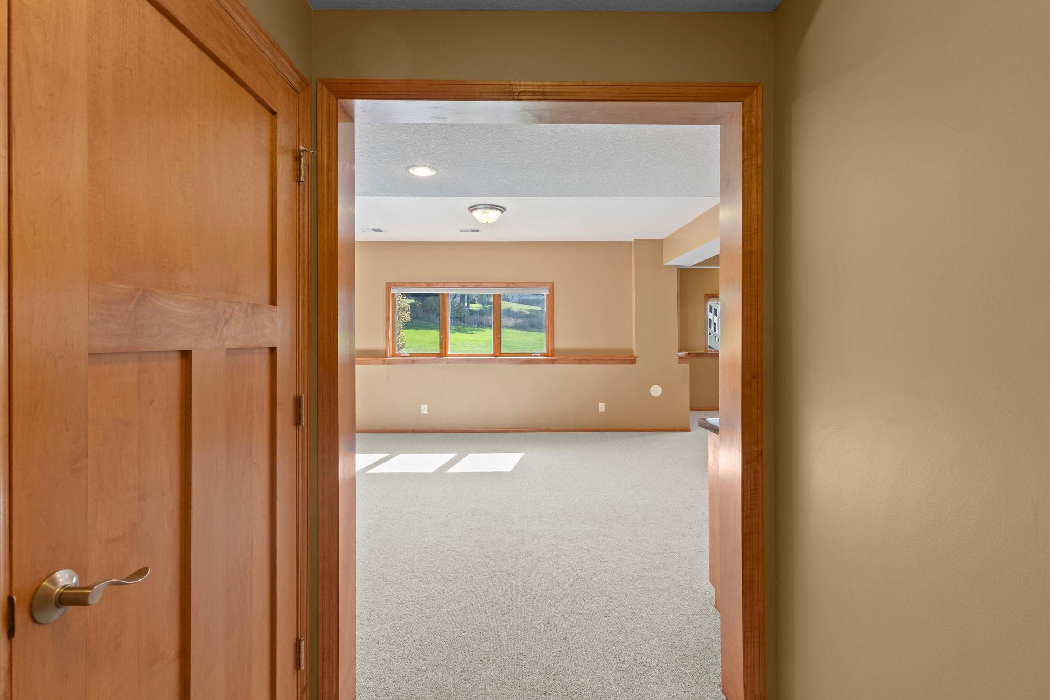 Vacant carpeted room with tan walls, wood trim, and a wide window overlooking a lawn.
