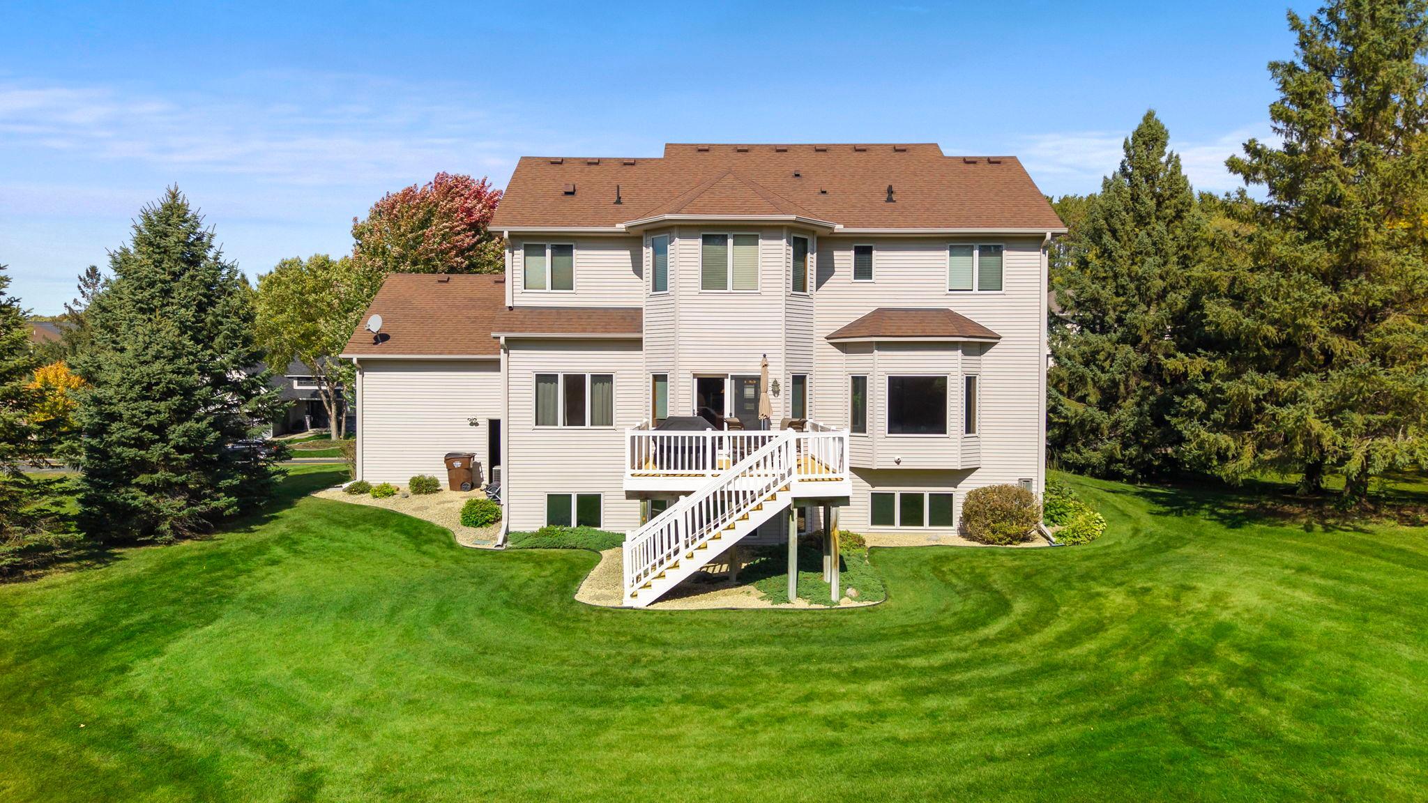 Rear of a two-story home with a raised white deck, stairs, and broad green lawn.