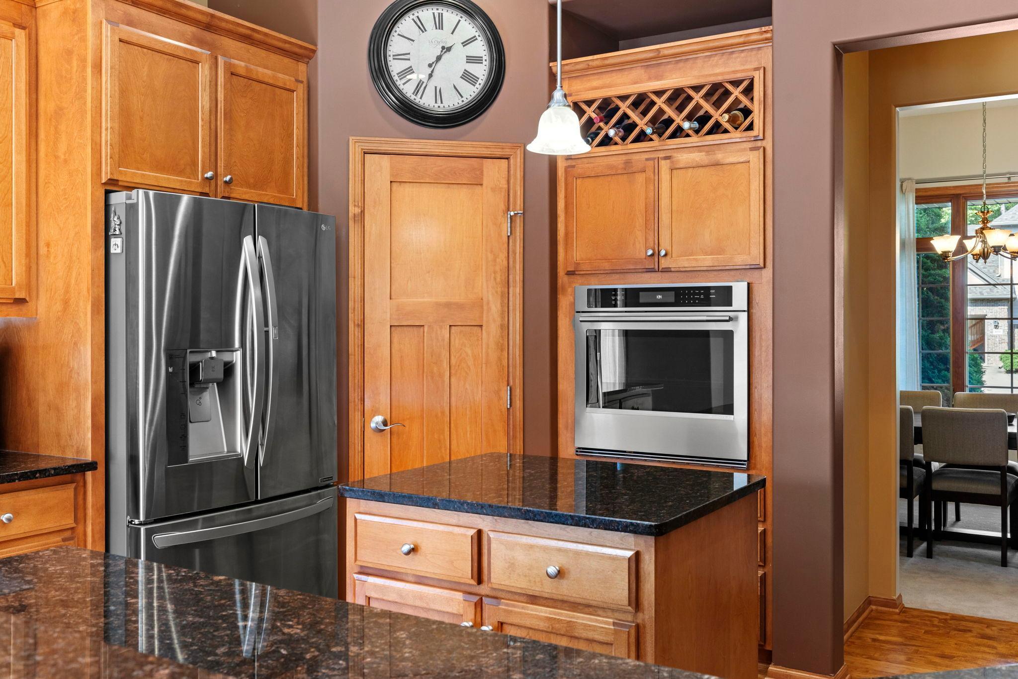 Kitchen with warm wood cabinetry, granite countertops, stainless appliances, and an overhead wine rack.