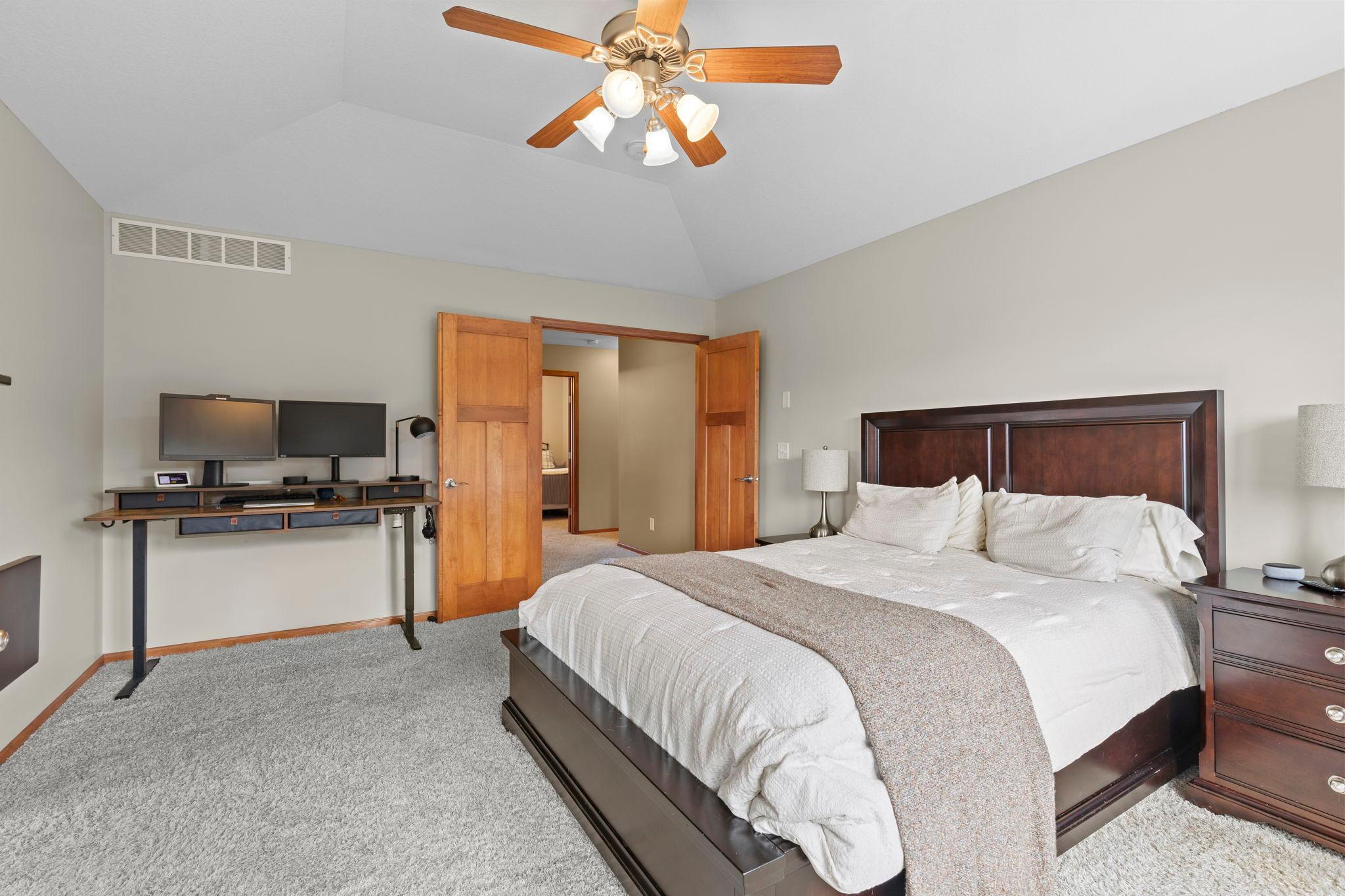 Bedroom with a large dark wood bed, vaulted ceiling, and desk with dual monitors.
