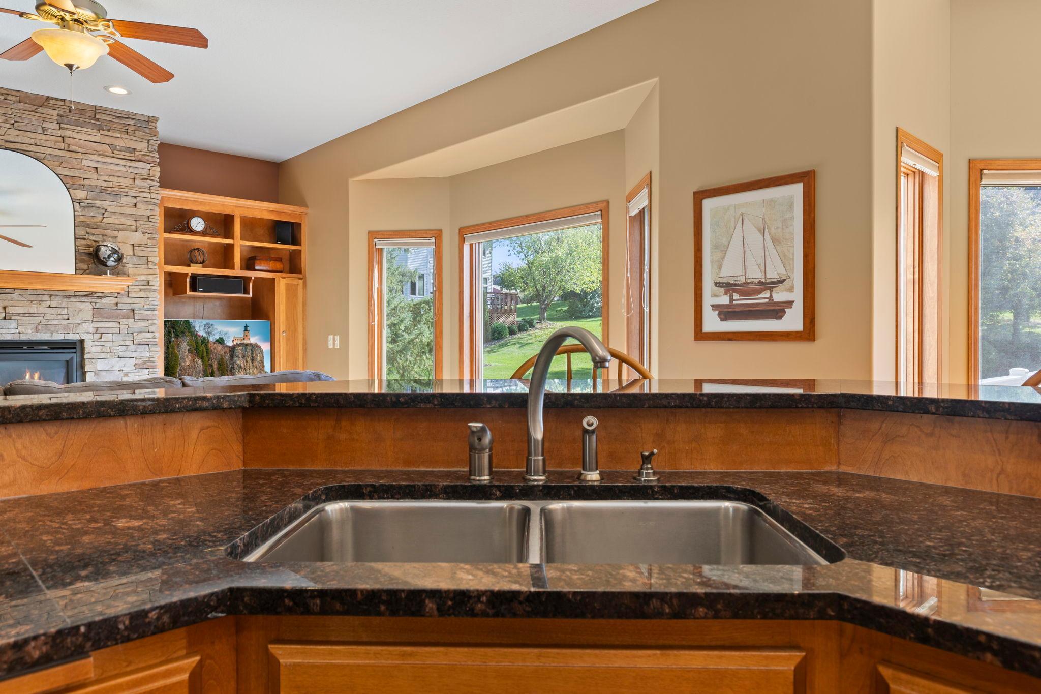 Kitchen with a double-basin sink, granite counters, and views of a stone fireplace and green yard.