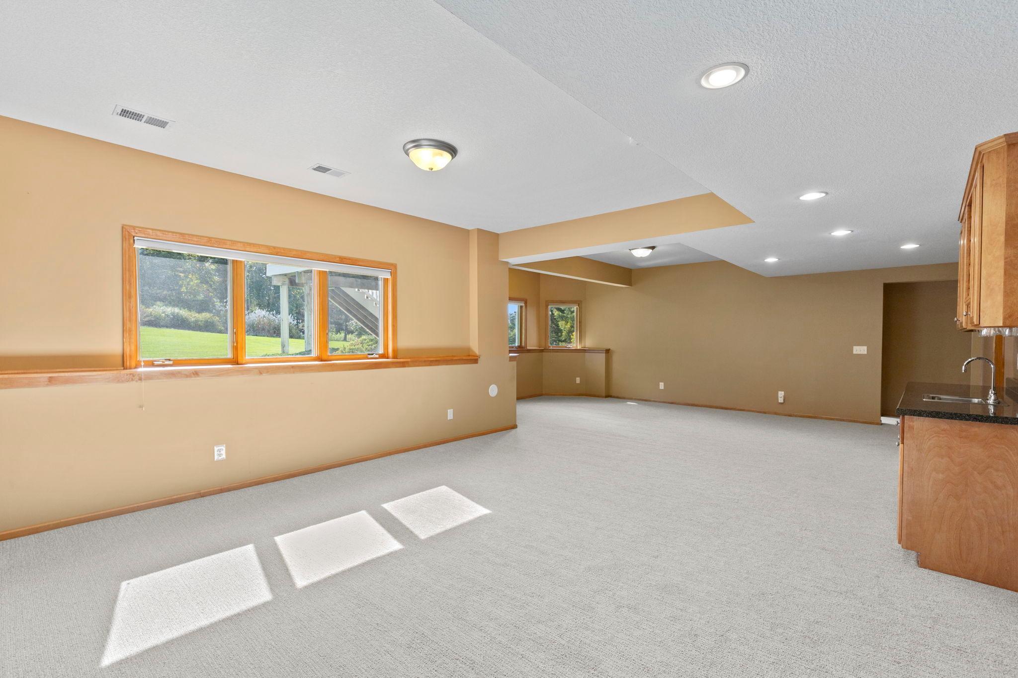 Empty carpeted living area with wood-trimmed windows and a partial kitchenette at the right.
