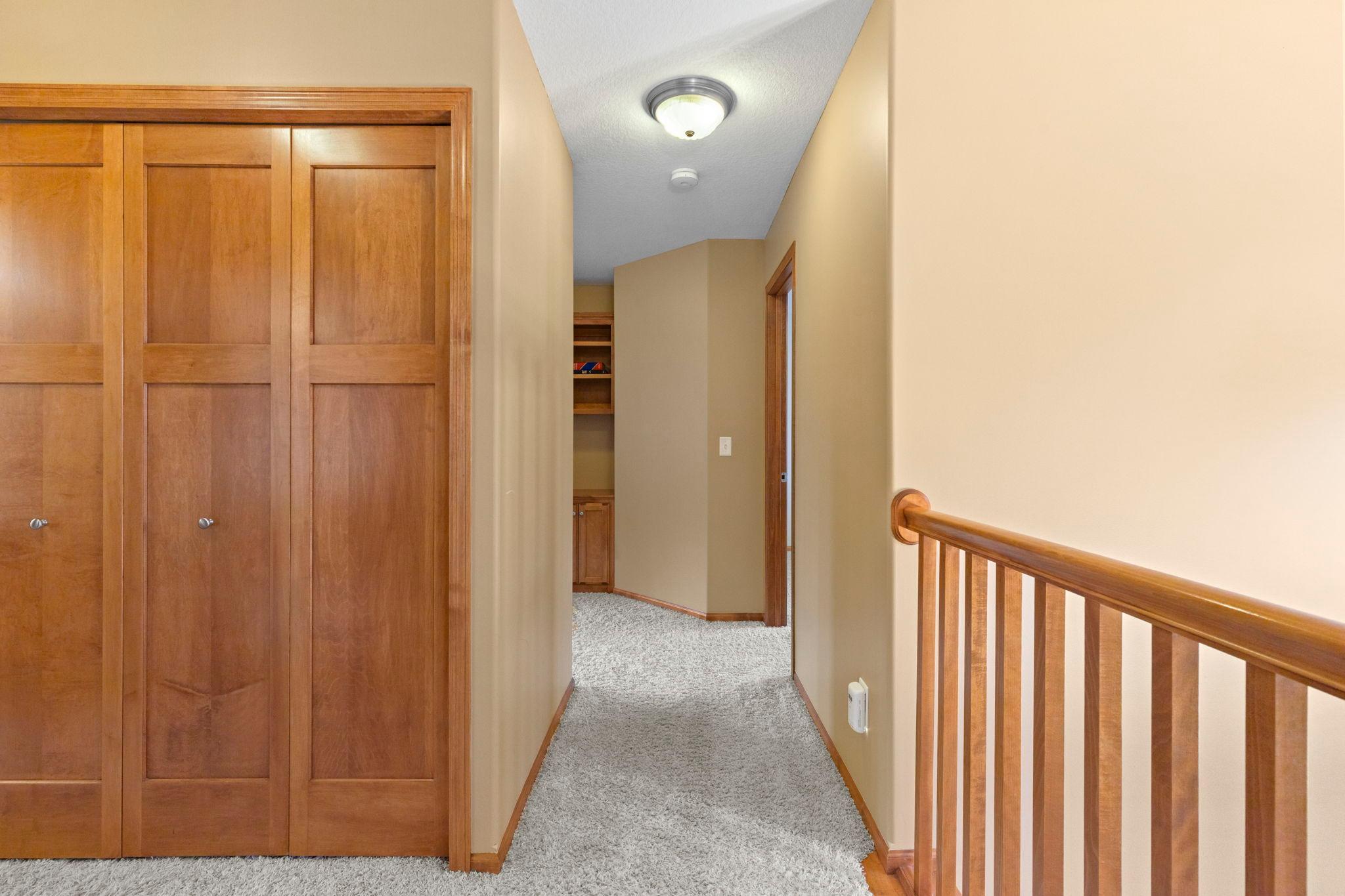 Upstairs hallway with paneled wood closet doors, gray carpet, and a matching stair railing.