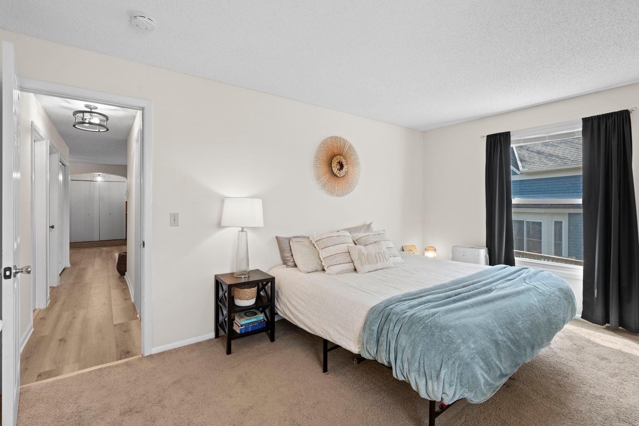 Bedroom with a white bed, pale blue throw, black curtains, and an open hallway entrance.