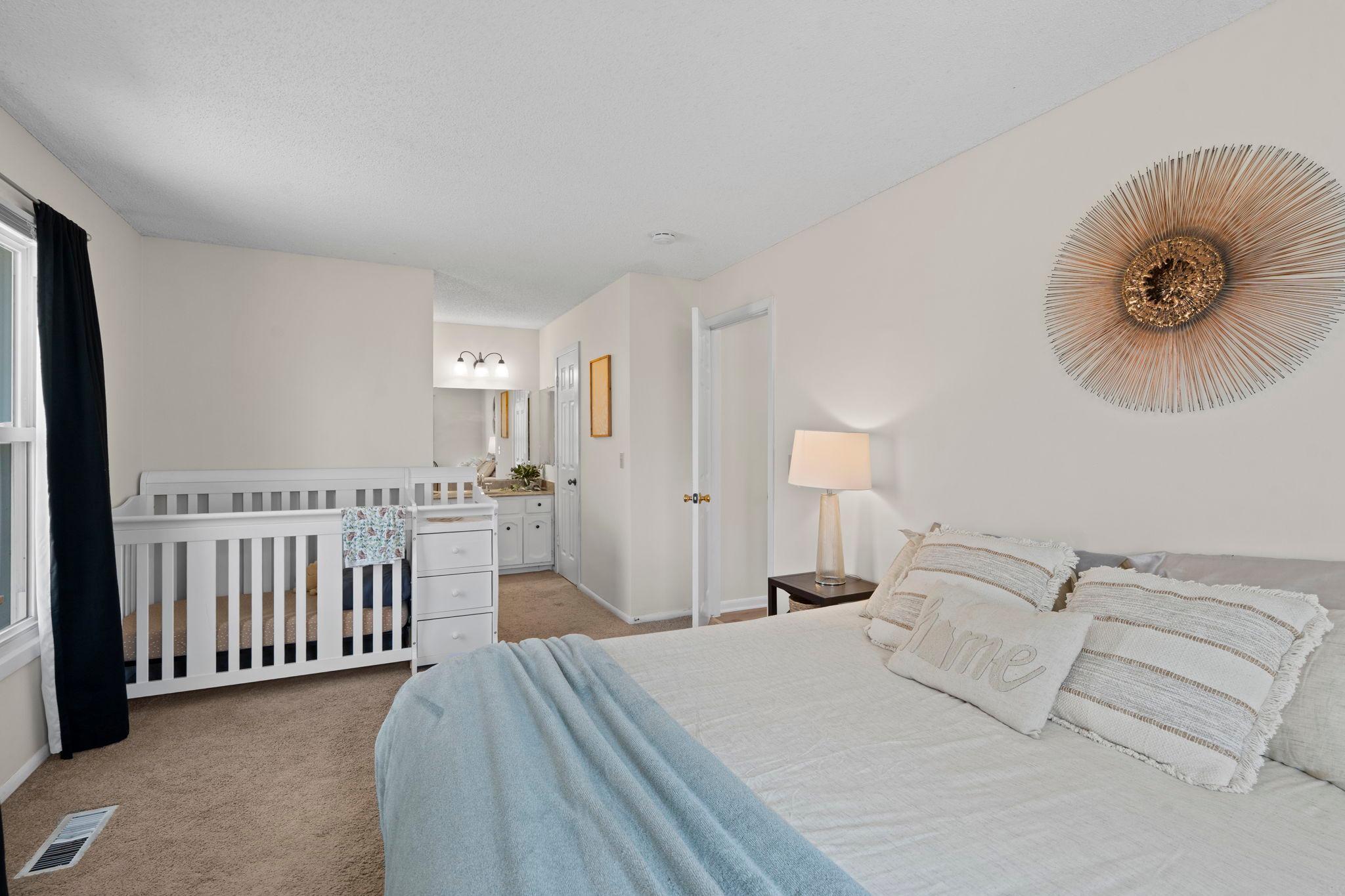 Bedroom with a white crib beside the bed, blue throw, and gold sunburst wall decor.
