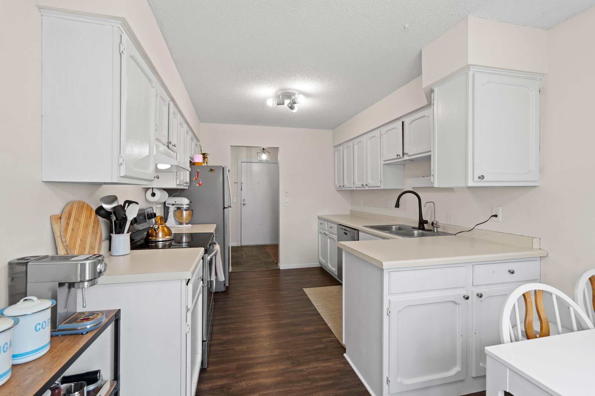 Kitchen with white cabinets, a peninsula, double-basin sink, and dark wood flooring.