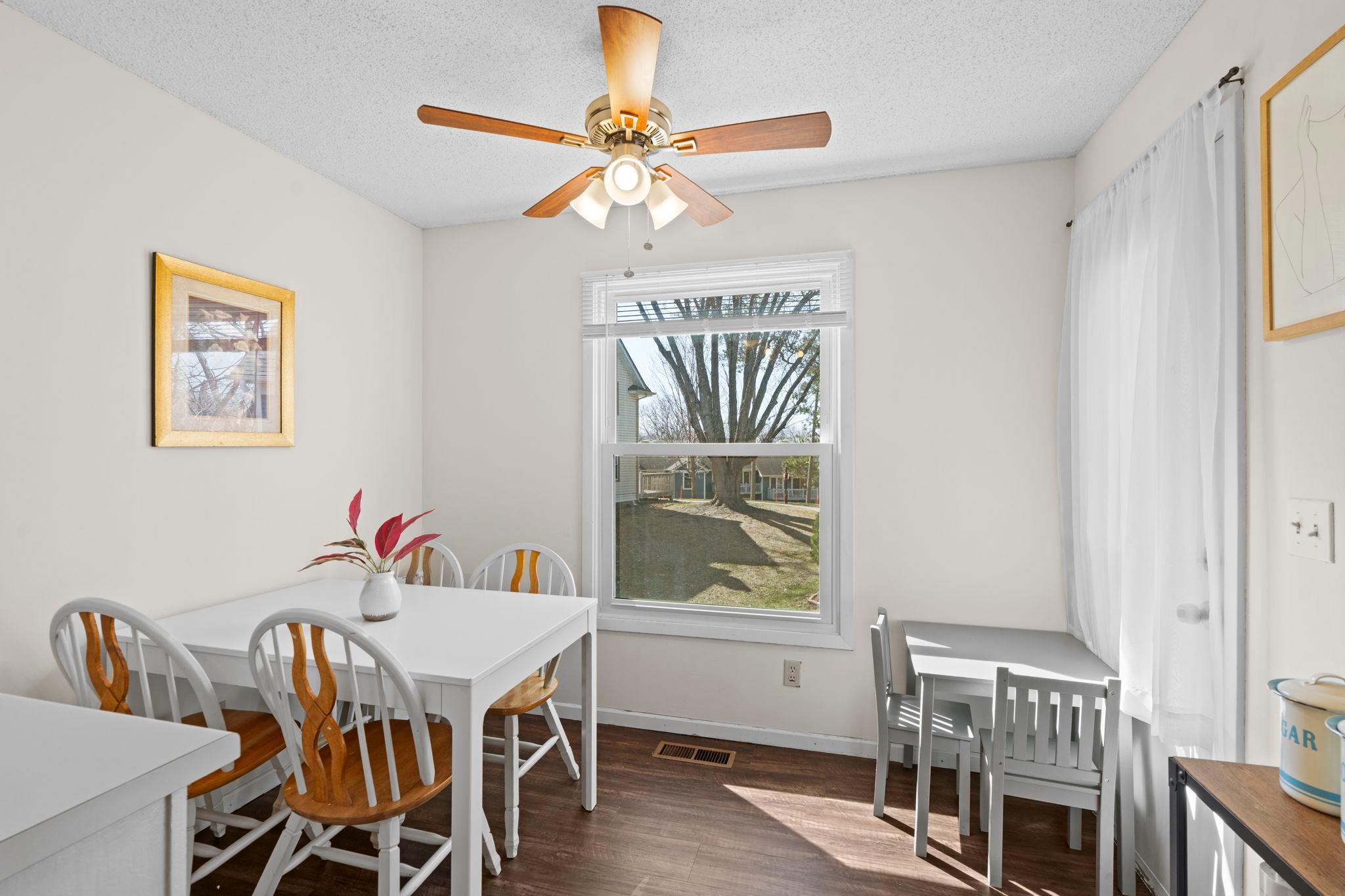 Dining room with a white table, wood-accented chairs, and a large courtyard-facing window.