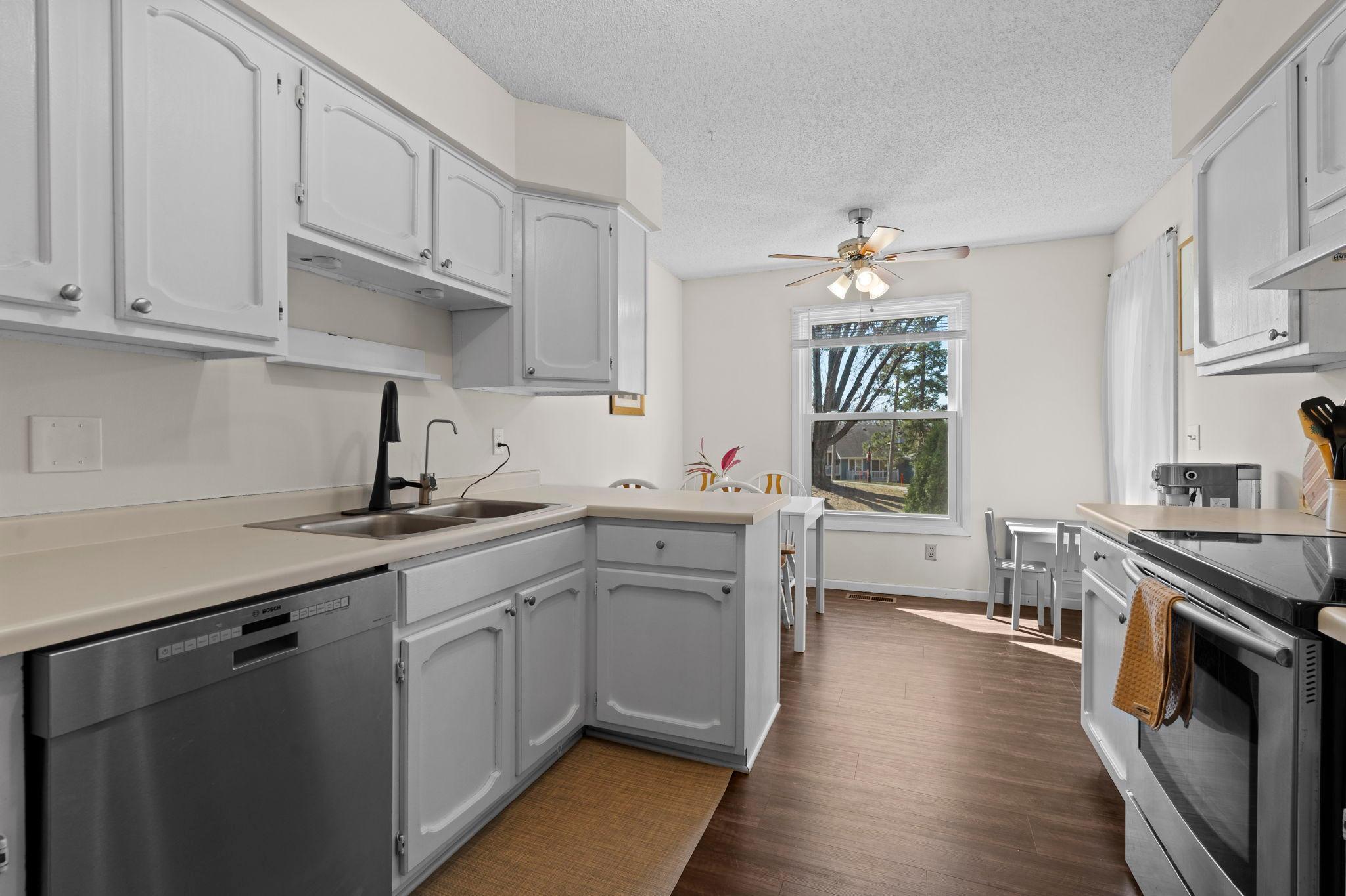 Kitchen with white cabinets and stainless steel appliances, opening to a window-side dining area.