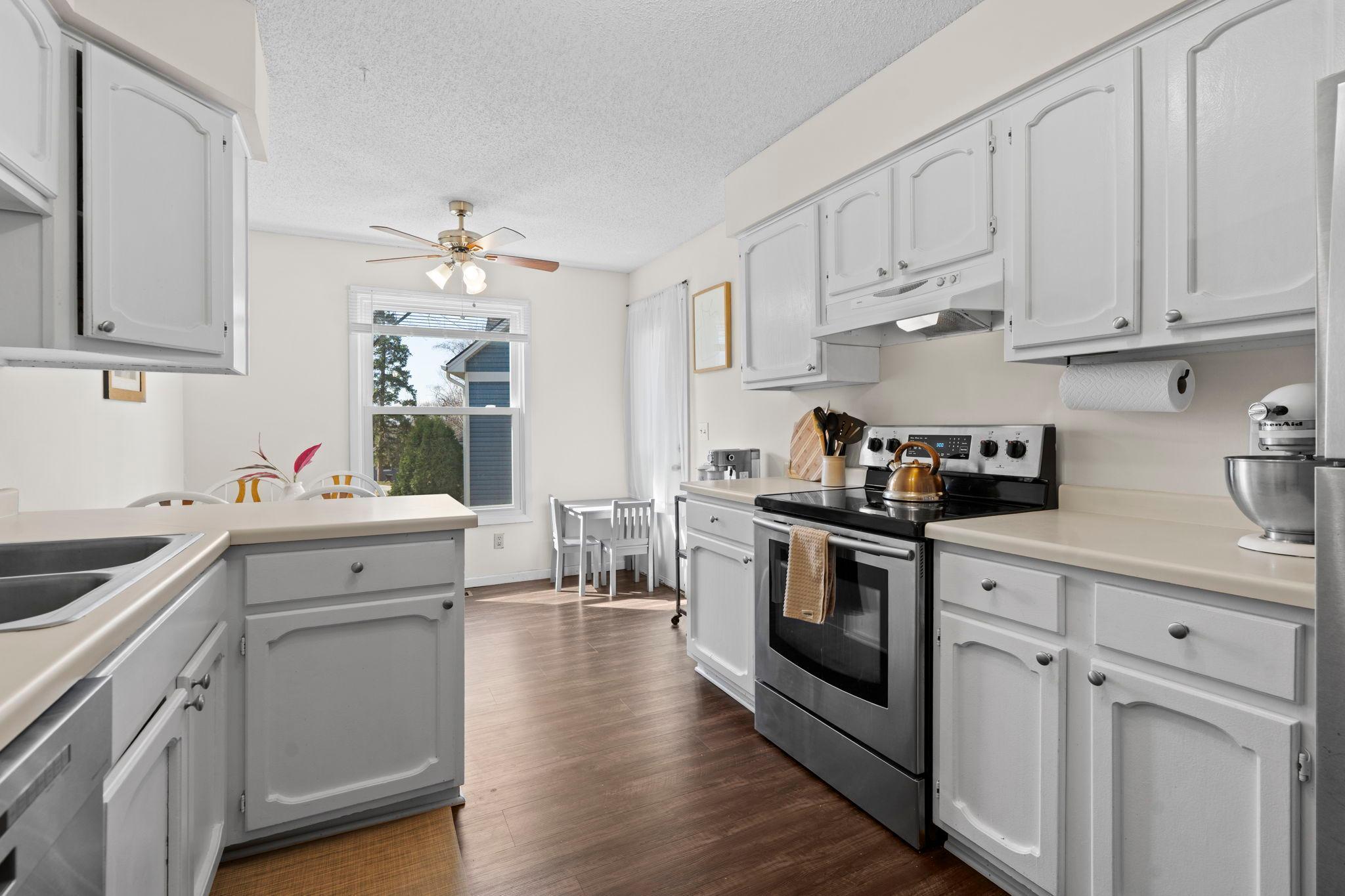 Bright white-cabinet kitchen with stainless appliances, an island, and a small dining nook by the window.