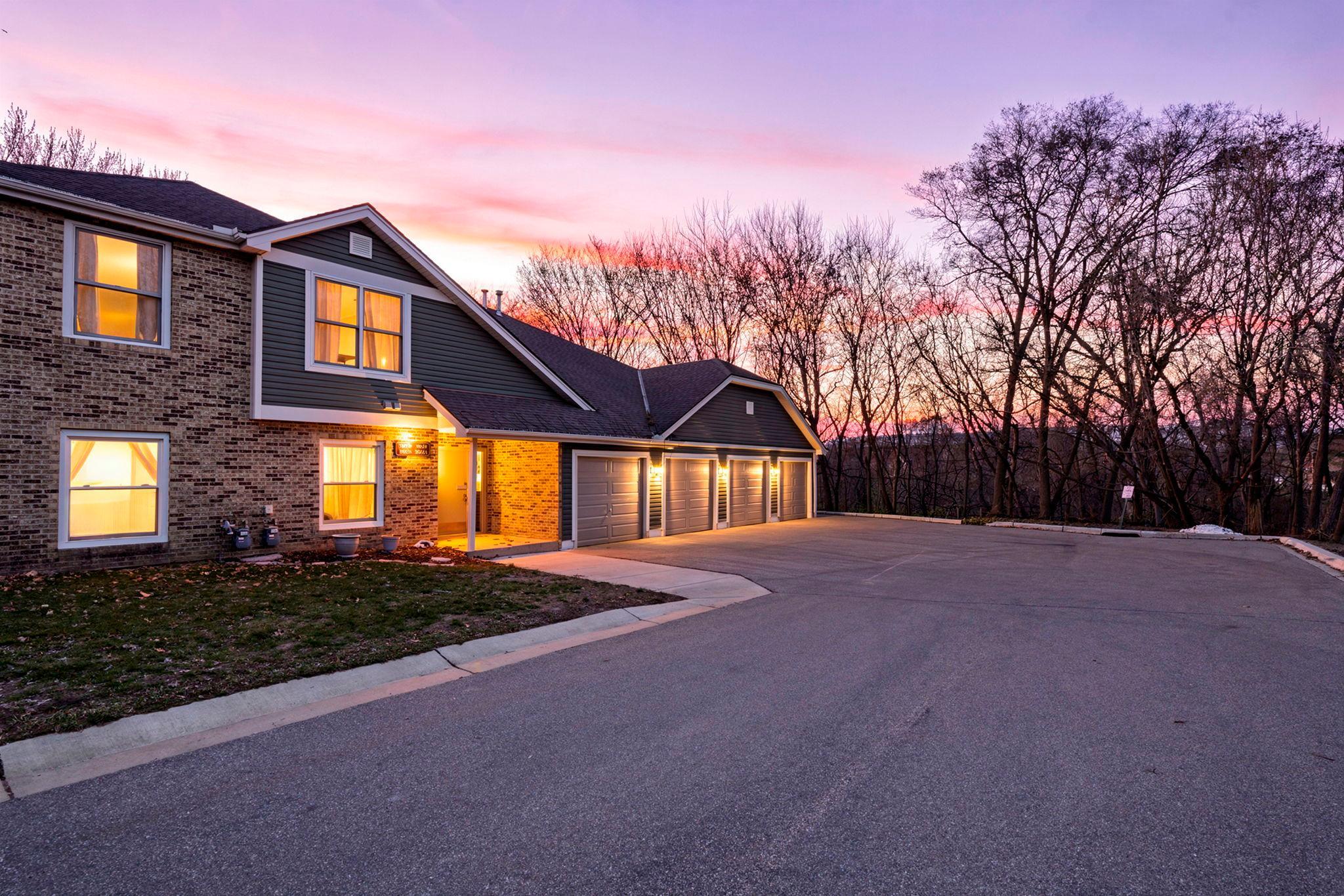 Brick residential building with lit windows and attached garages beneath a pink dusk sky.