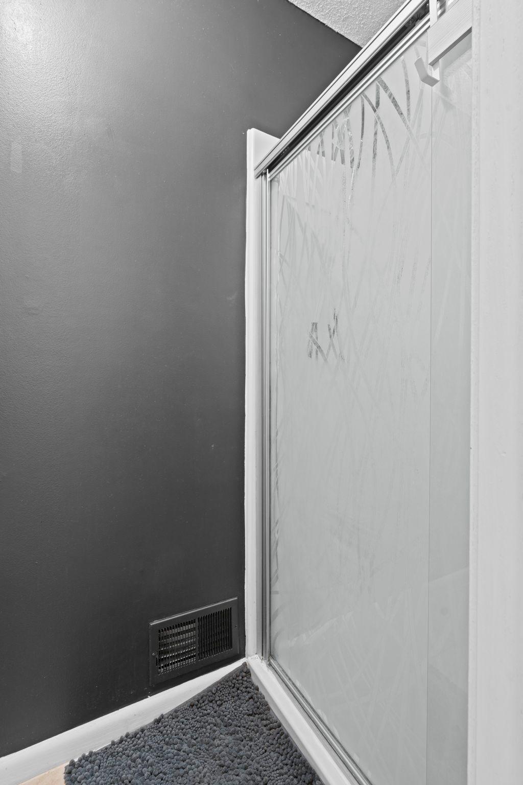 Glass shower enclosure beside a dark wall, with a pebble floor.