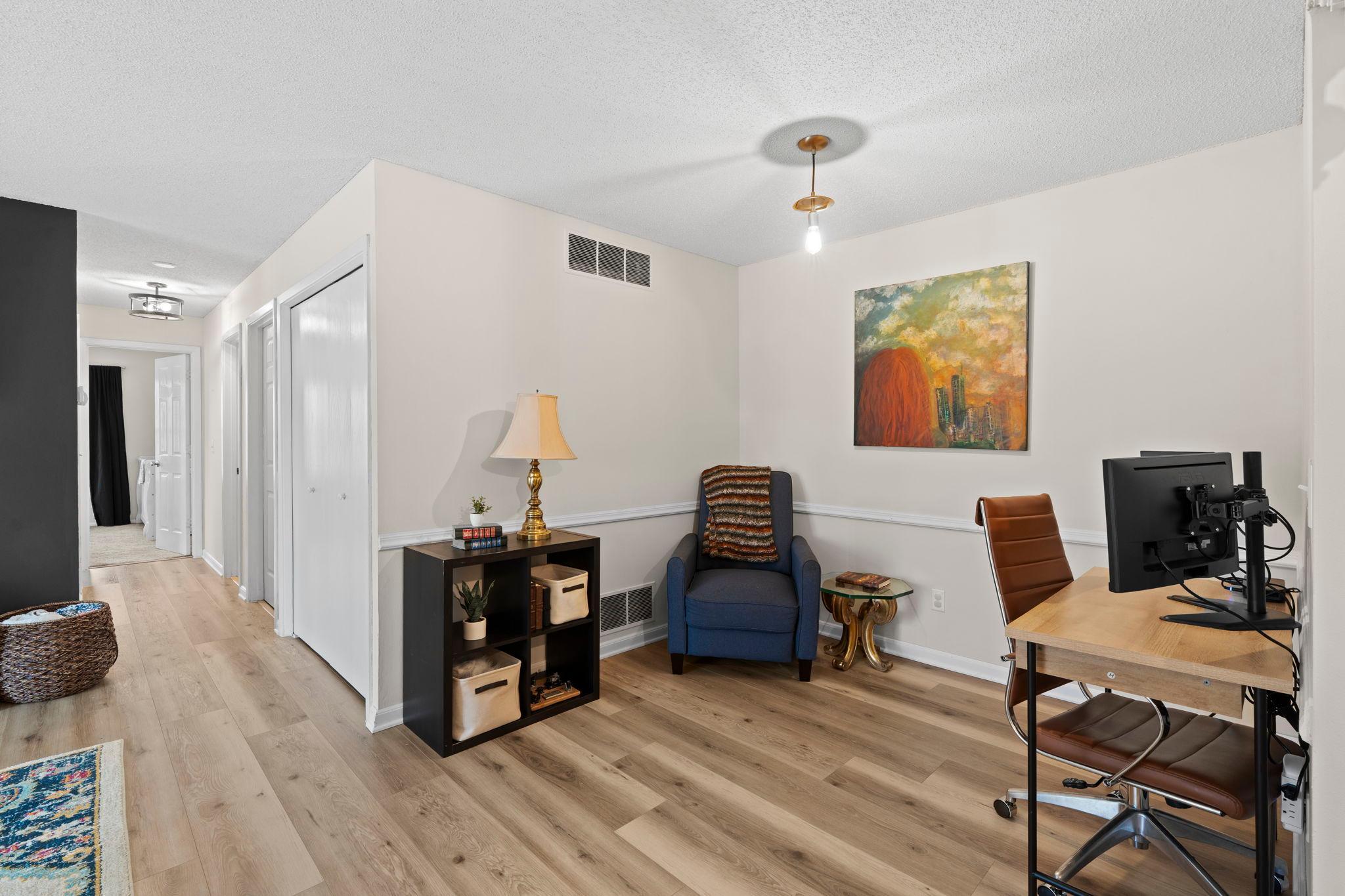 Furnished home office with a desk and computer, blue armchair, and light wood floors.
