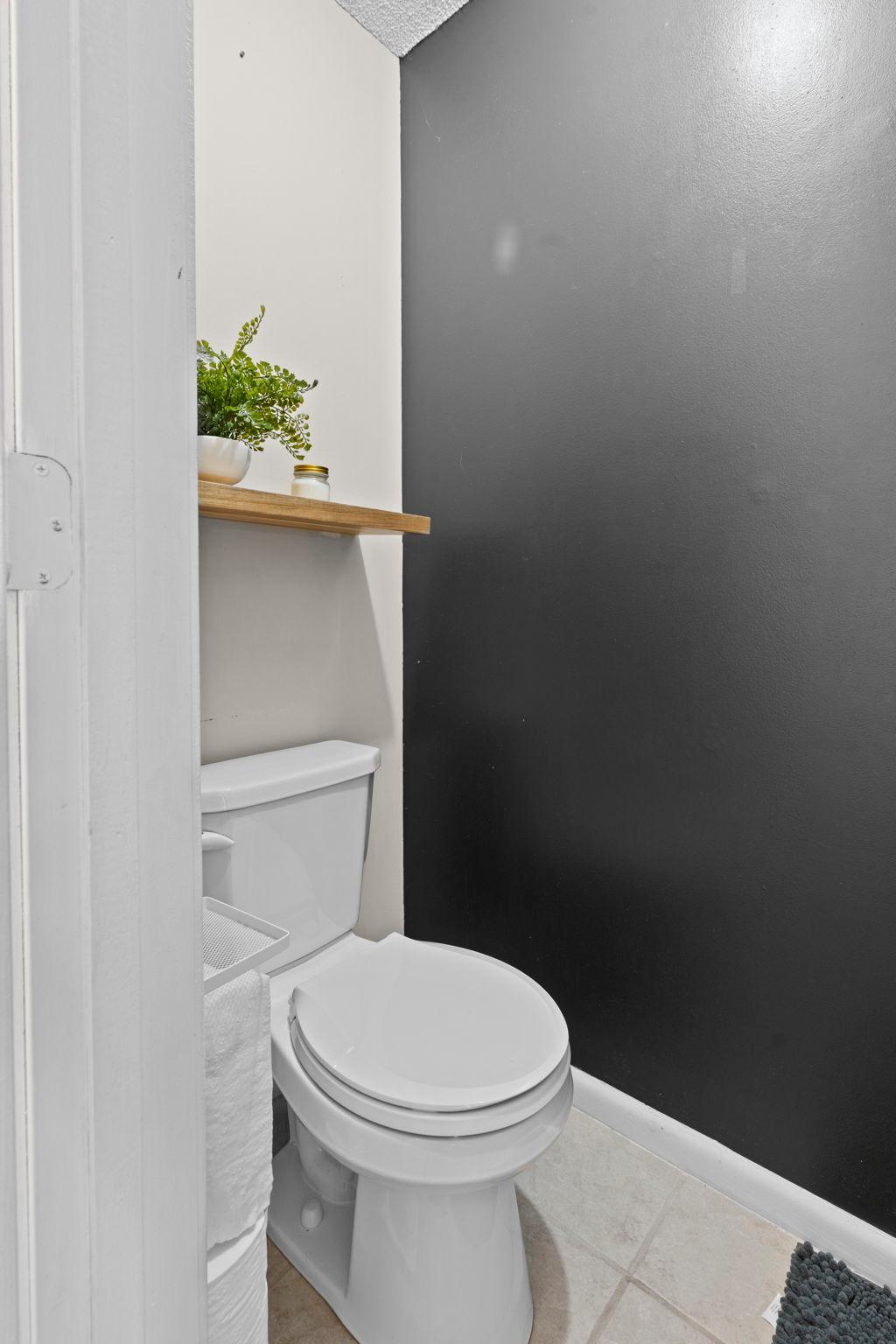 Bathroom with a white toilet, charcoal accent wall, and wood shelf with greenery.