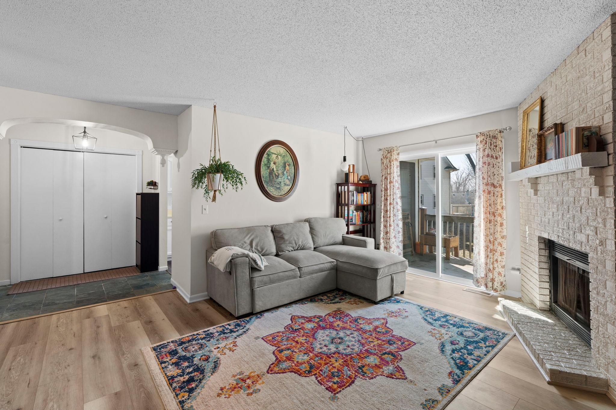 Living room with a gray sectional, white brick fireplace, sliding doors to a deck, and colorful patterned rug.