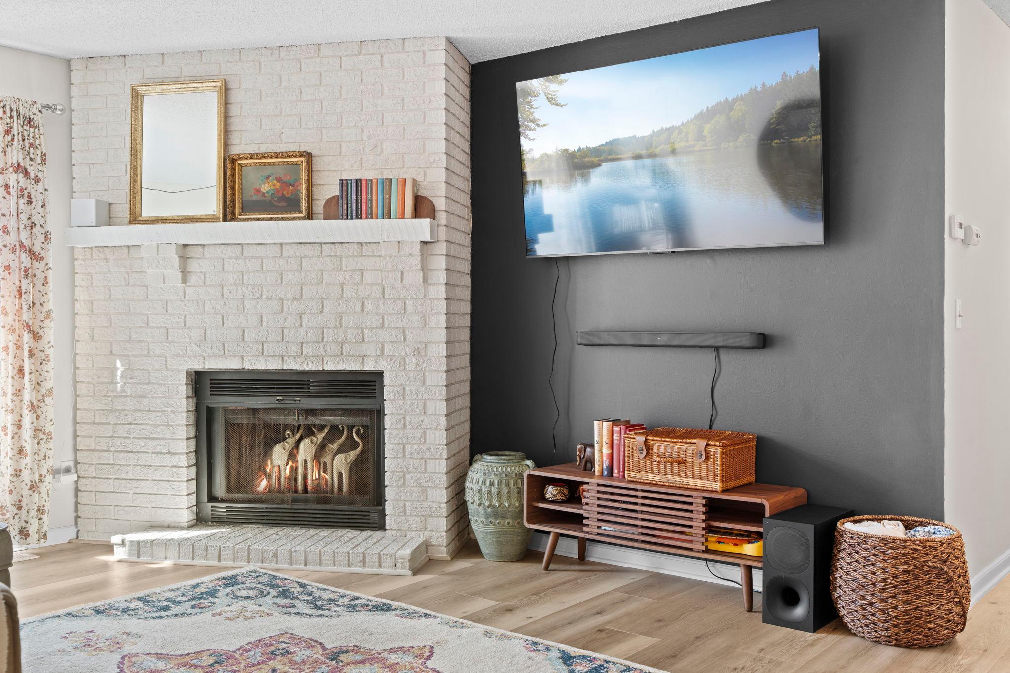 Living room with a white brick fireplace, lit fire, and television above a wooden media console.