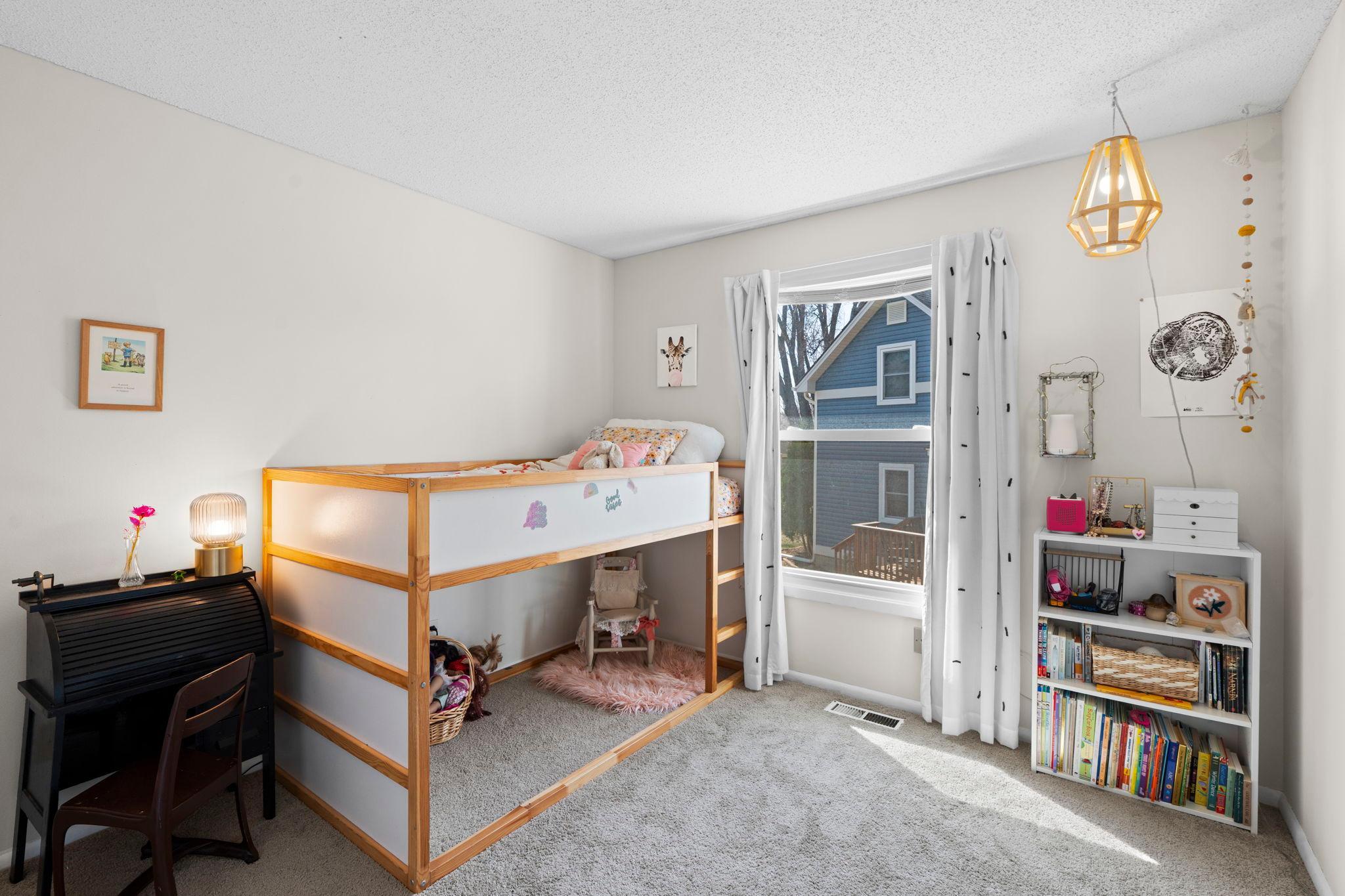 Child's bedroom with a wooden bunk bed, a desk, and a bookshelf of books and toys.