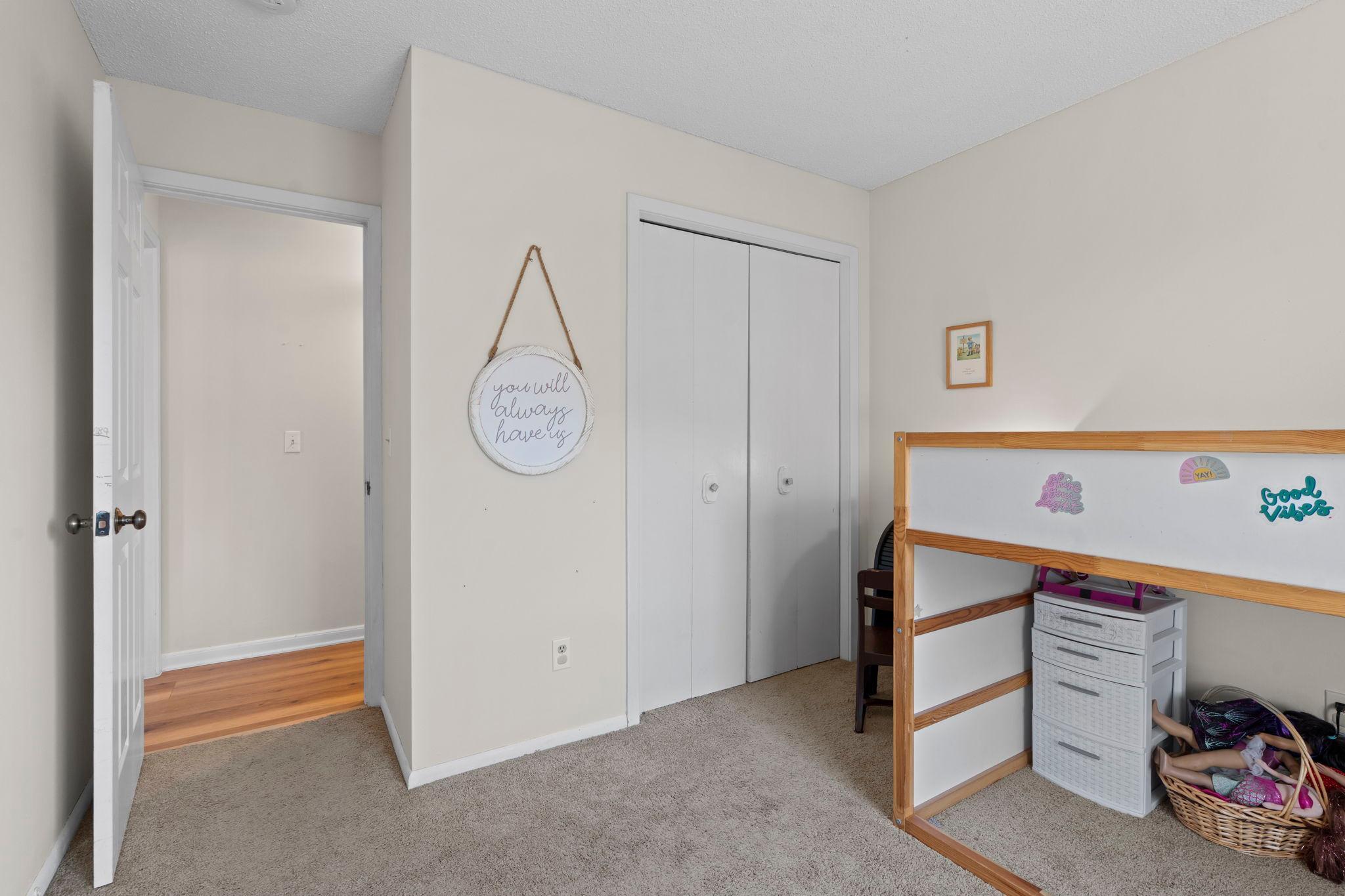 Bedroom with beige carpet, white closet doors, and a wooden bed frame beside children’s toys.