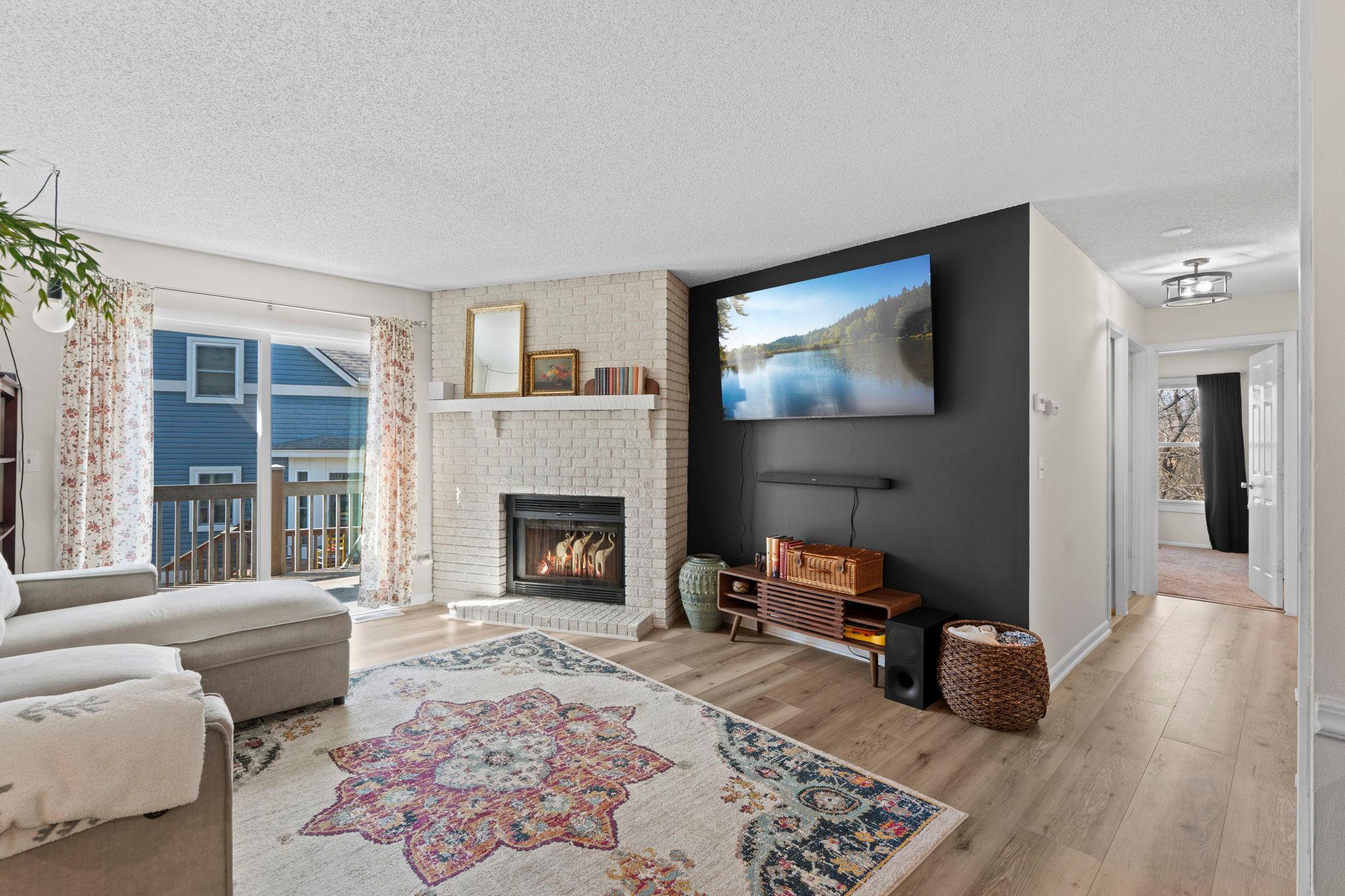 Living room with a white brick fireplace, dark TV wall, patterned rug, and sliding doors to a balcony.