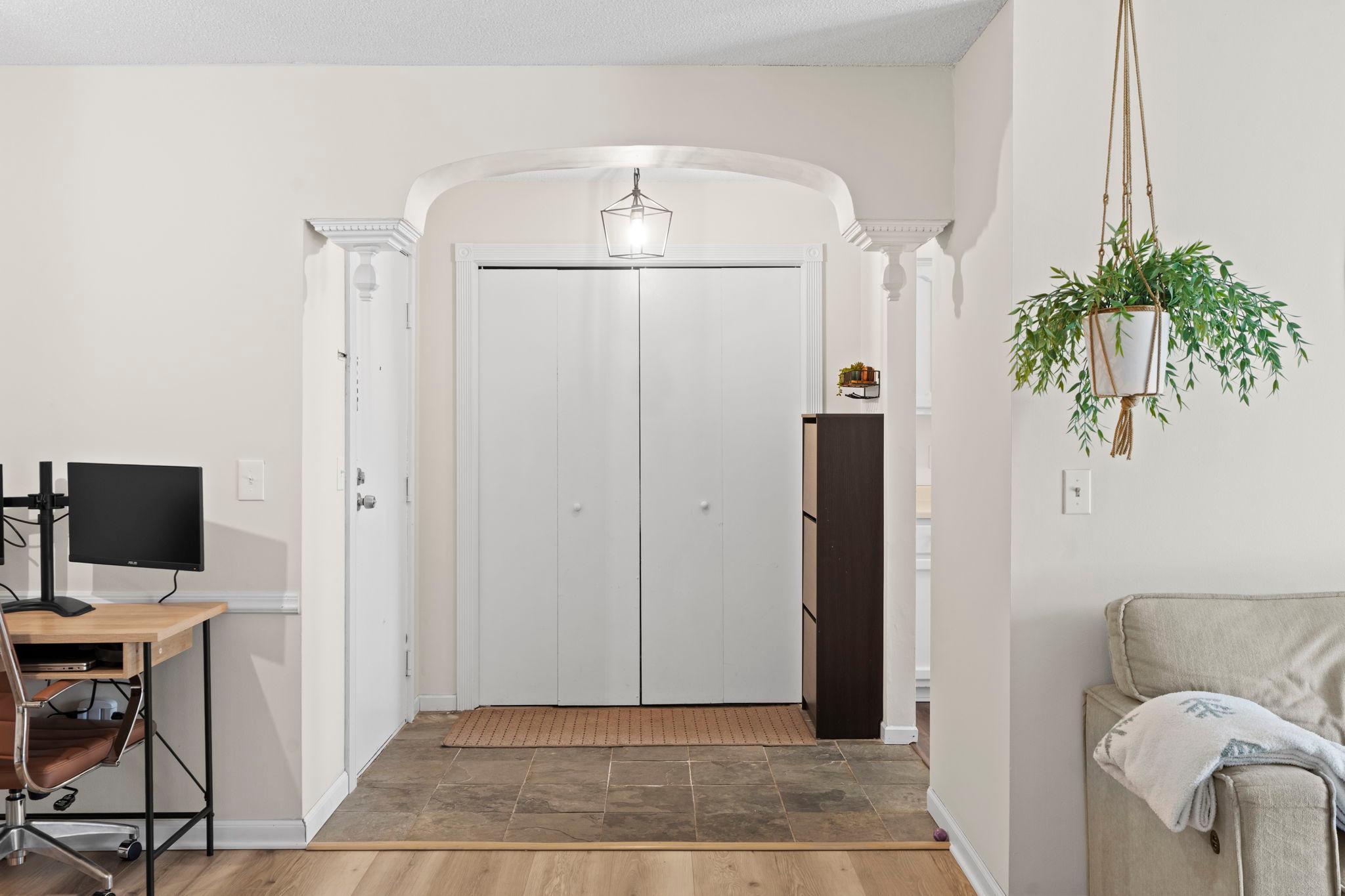 Condo entryway with an arched opening, tiled floor, double closet doors, and hanging plant.