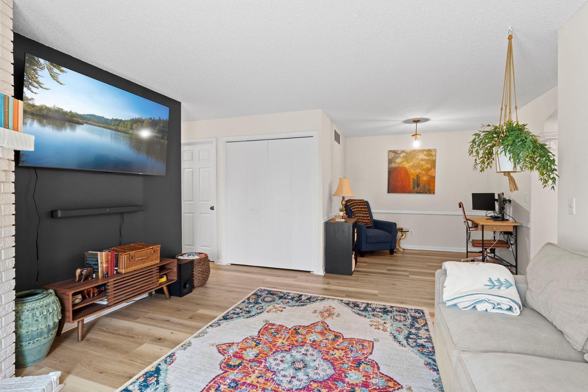 Furnished living room with a wall-mounted television, white brick fireplace, and desk workspace.
