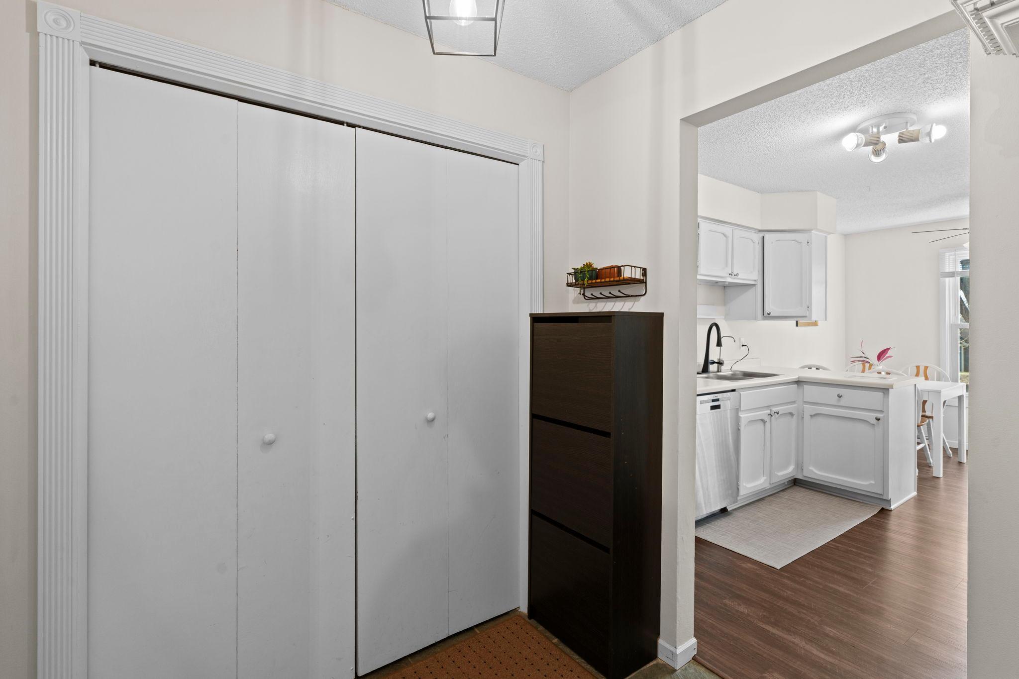 Entryway with white sliding closet doors and dark cabinet, opening to a bright kitchen.