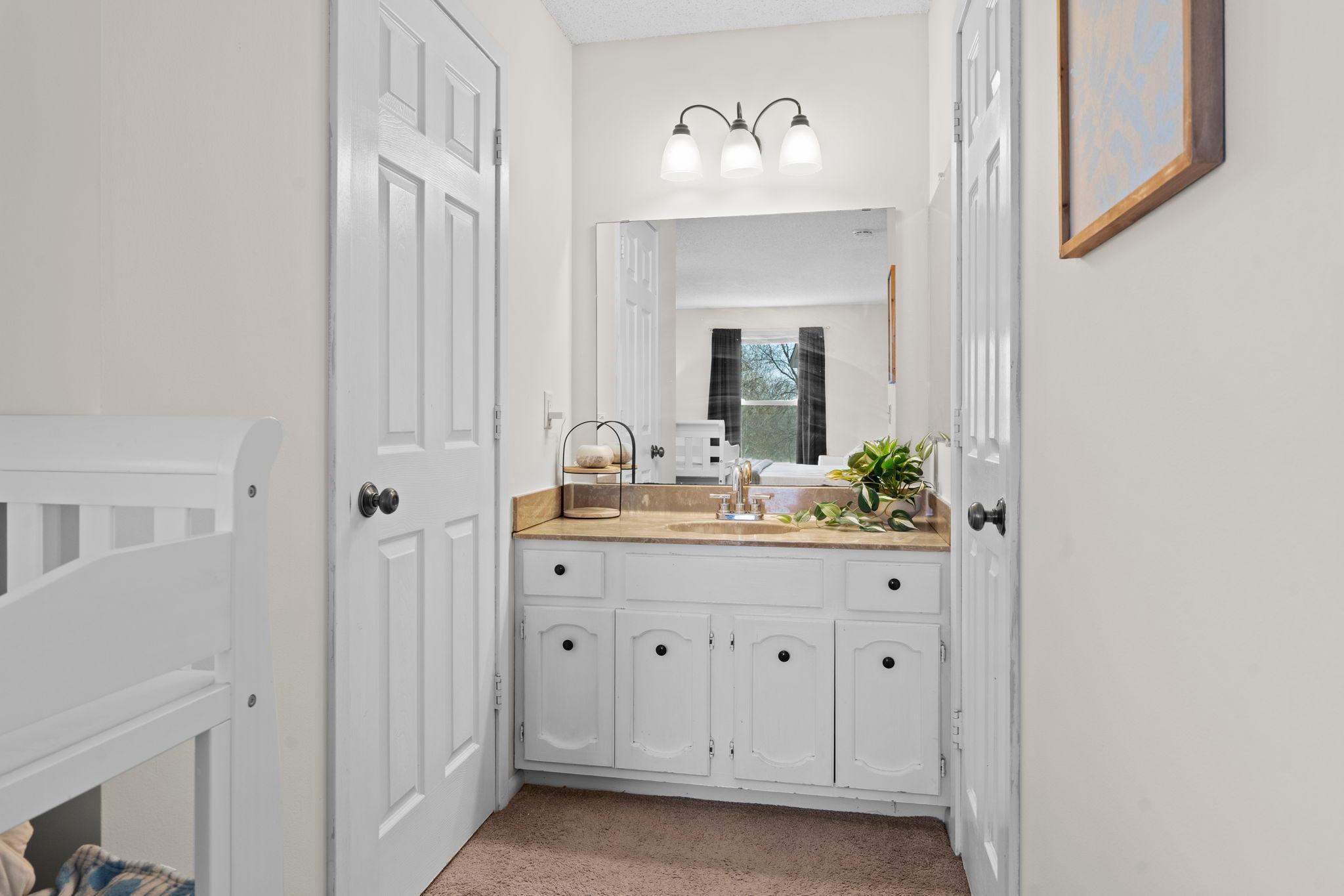 Bathroom vanity with tan countertop, white cabinets, large mirror, and a leafy plant beside the sink.