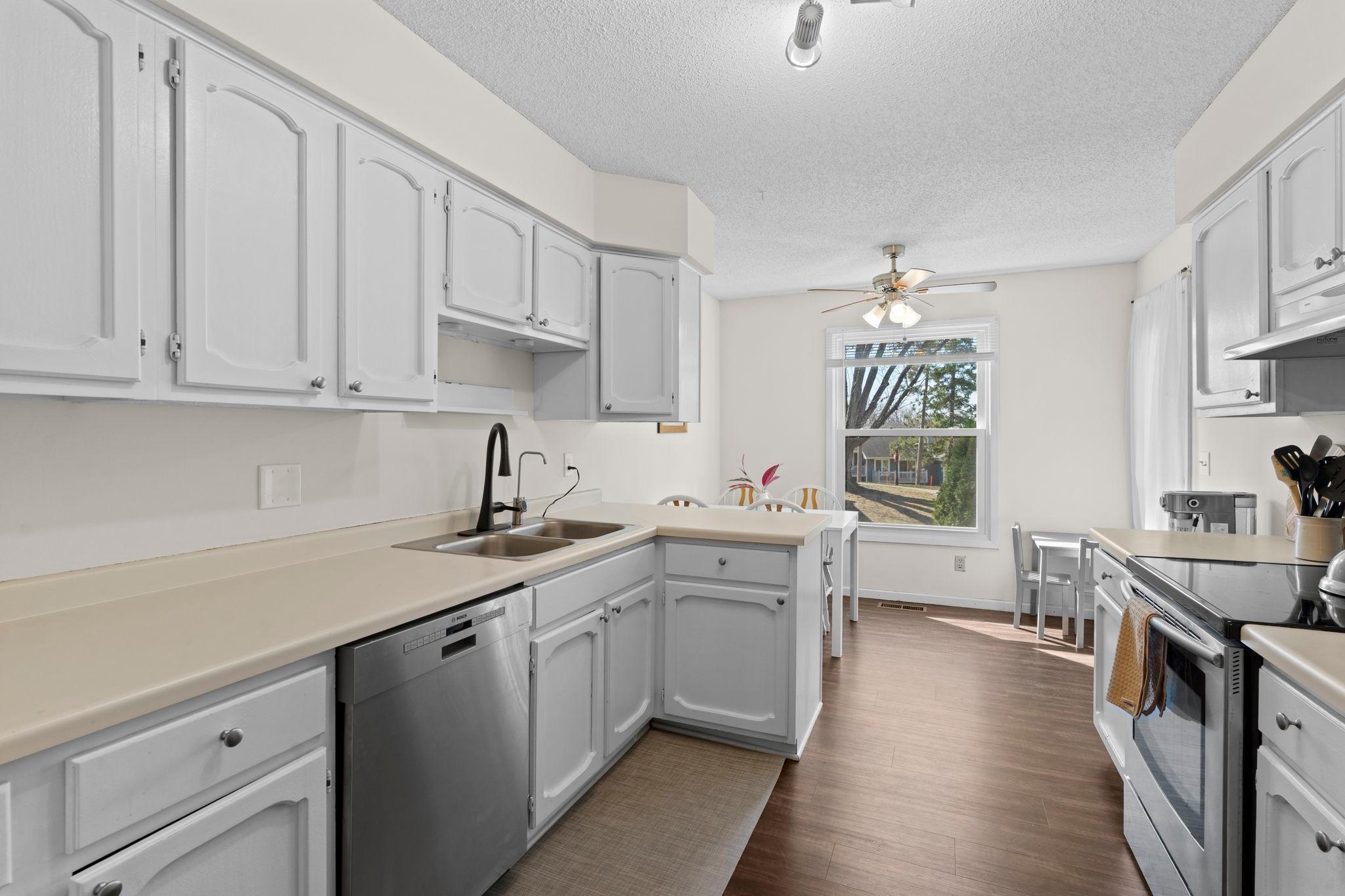 Kitchen with white cabinets, stainless steel appliances, and a dining area beside a window.