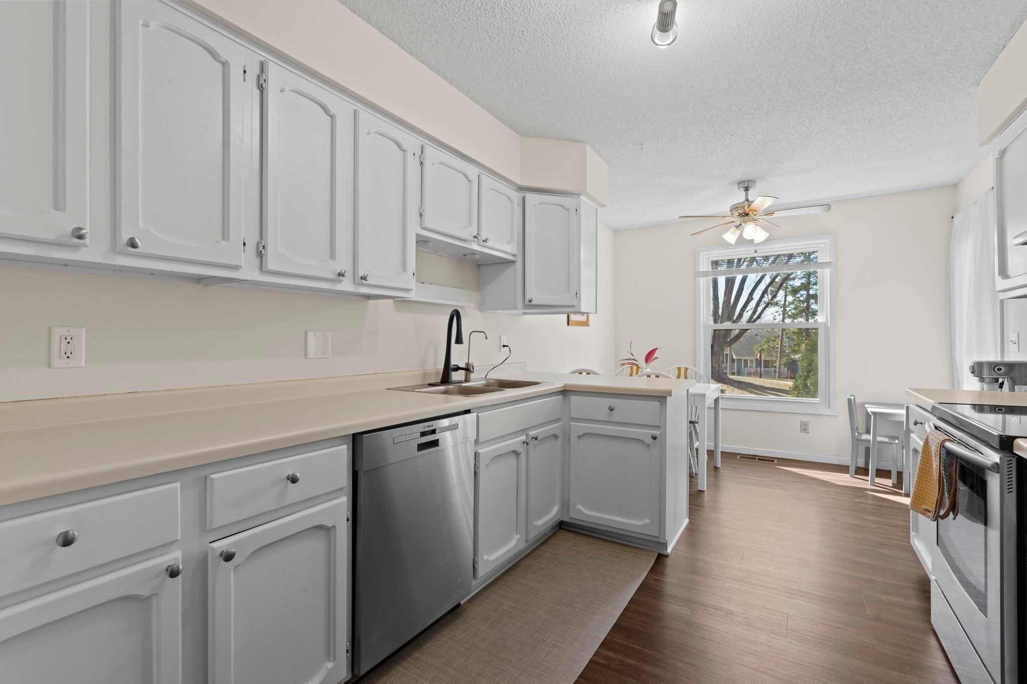 Kitchen with white cabinets, stainless steel appliances, and a dining area by a large window.