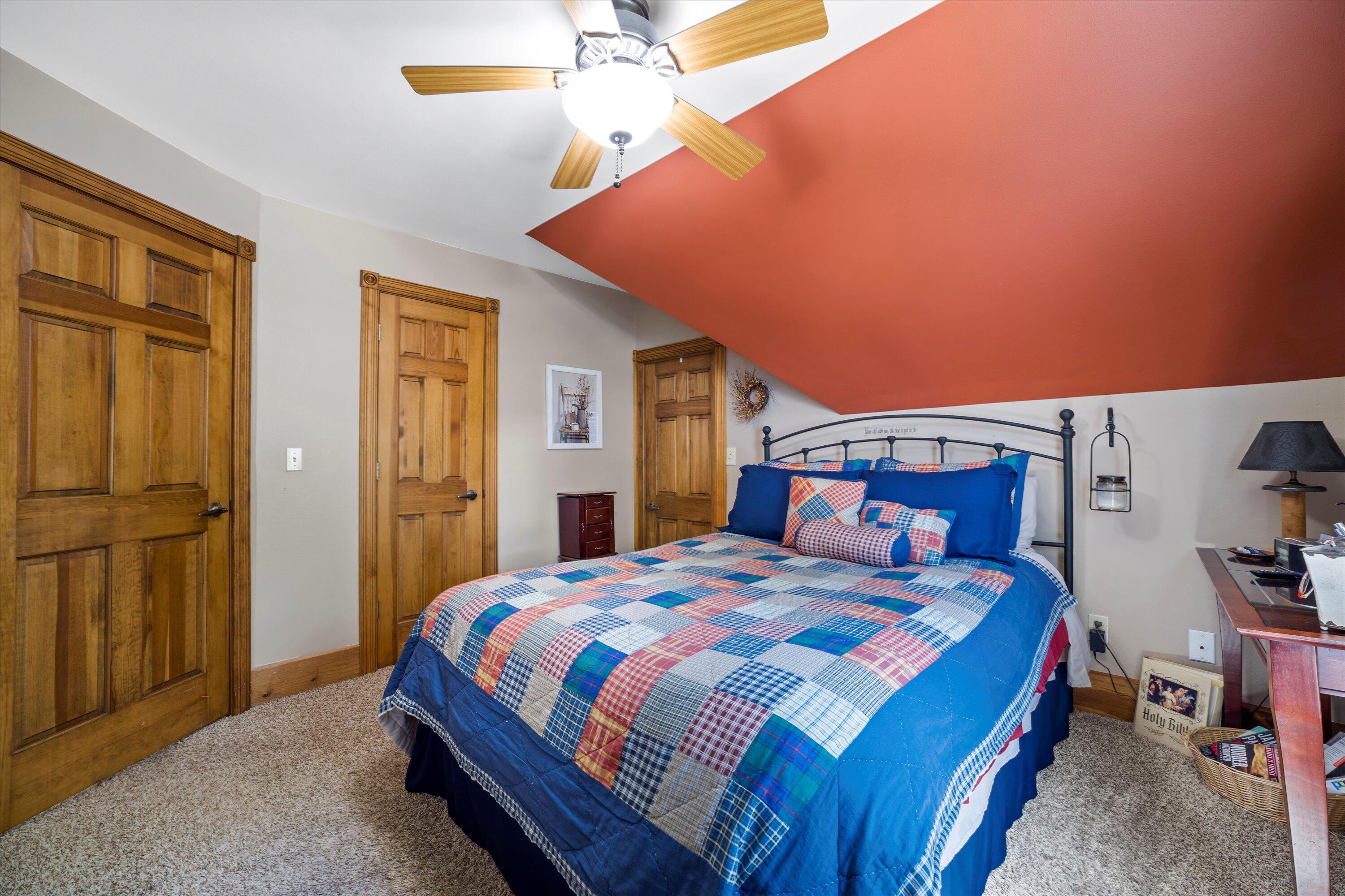 Bedroom with a blue patchwork bedspread beneath a red angled ceiling and ceiling fan.