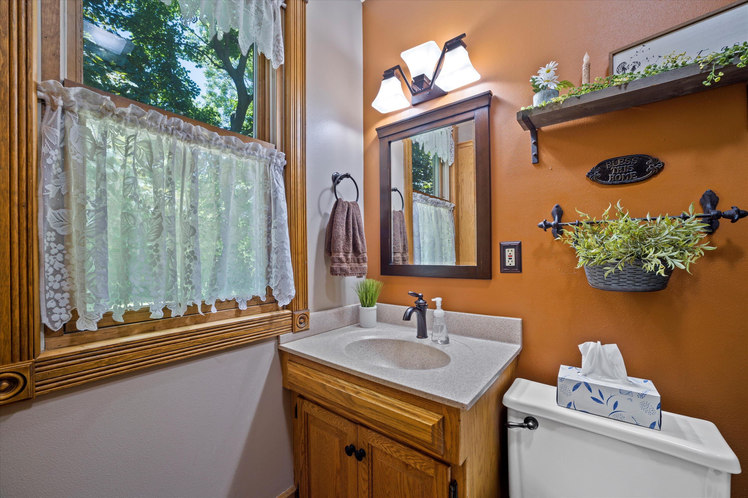 Bathroom with a wood vanity, lace-curtained window, and orange accent wall.