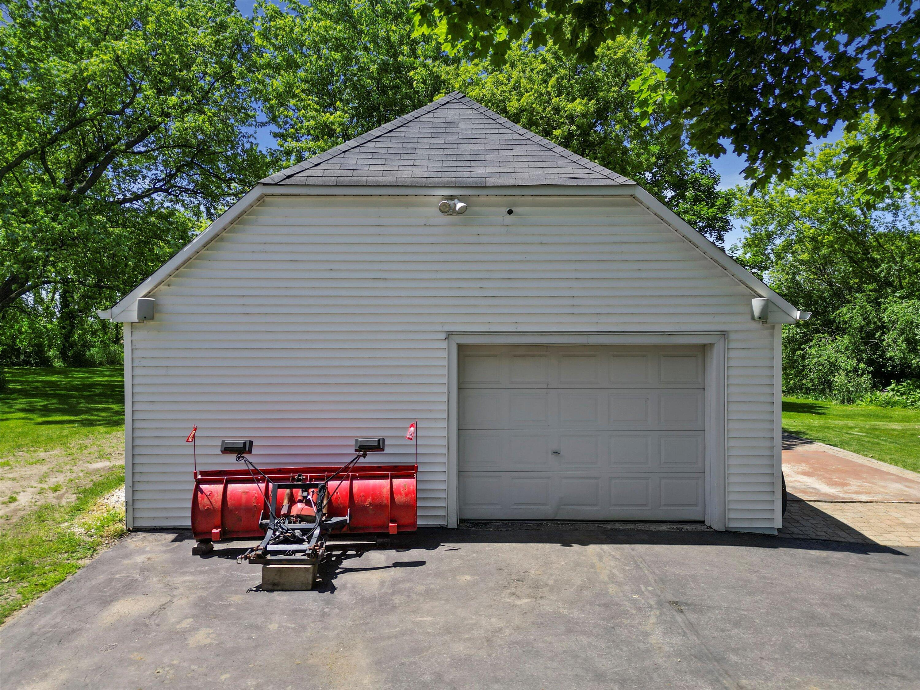 White detached garage with a red snowplow attachment parked in front.