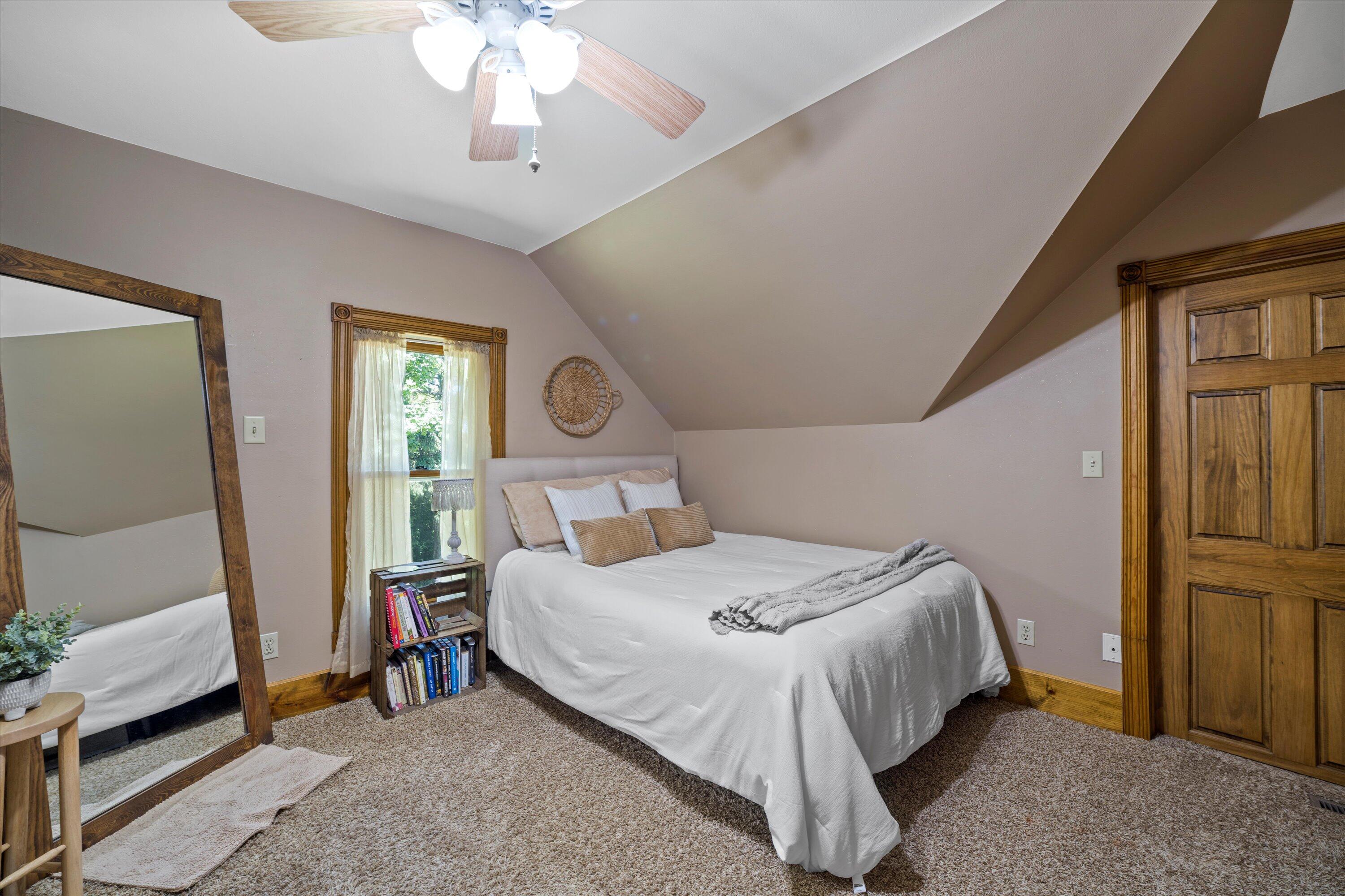 Furnished bedroom with a white bed beneath a sloped ceiling and a large wood-framed mirror.