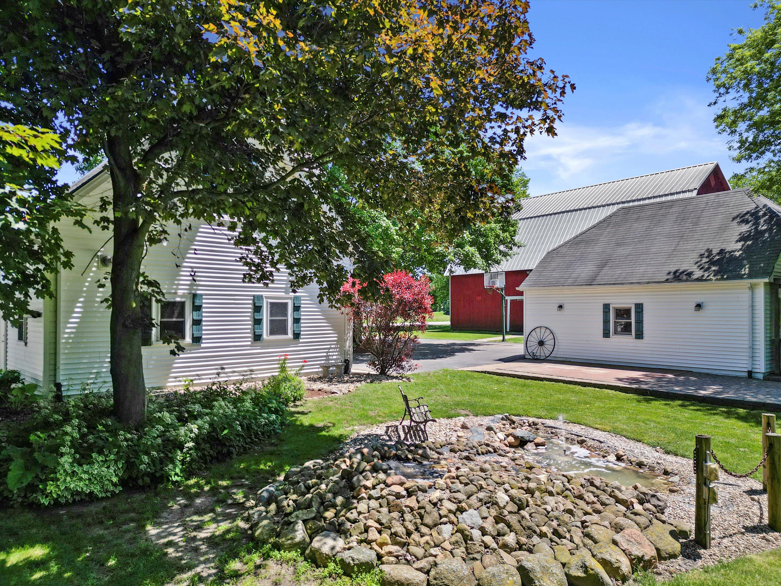 White-sided home and outbuildings beside a landscaped courtyard with a rock-lined water feature.