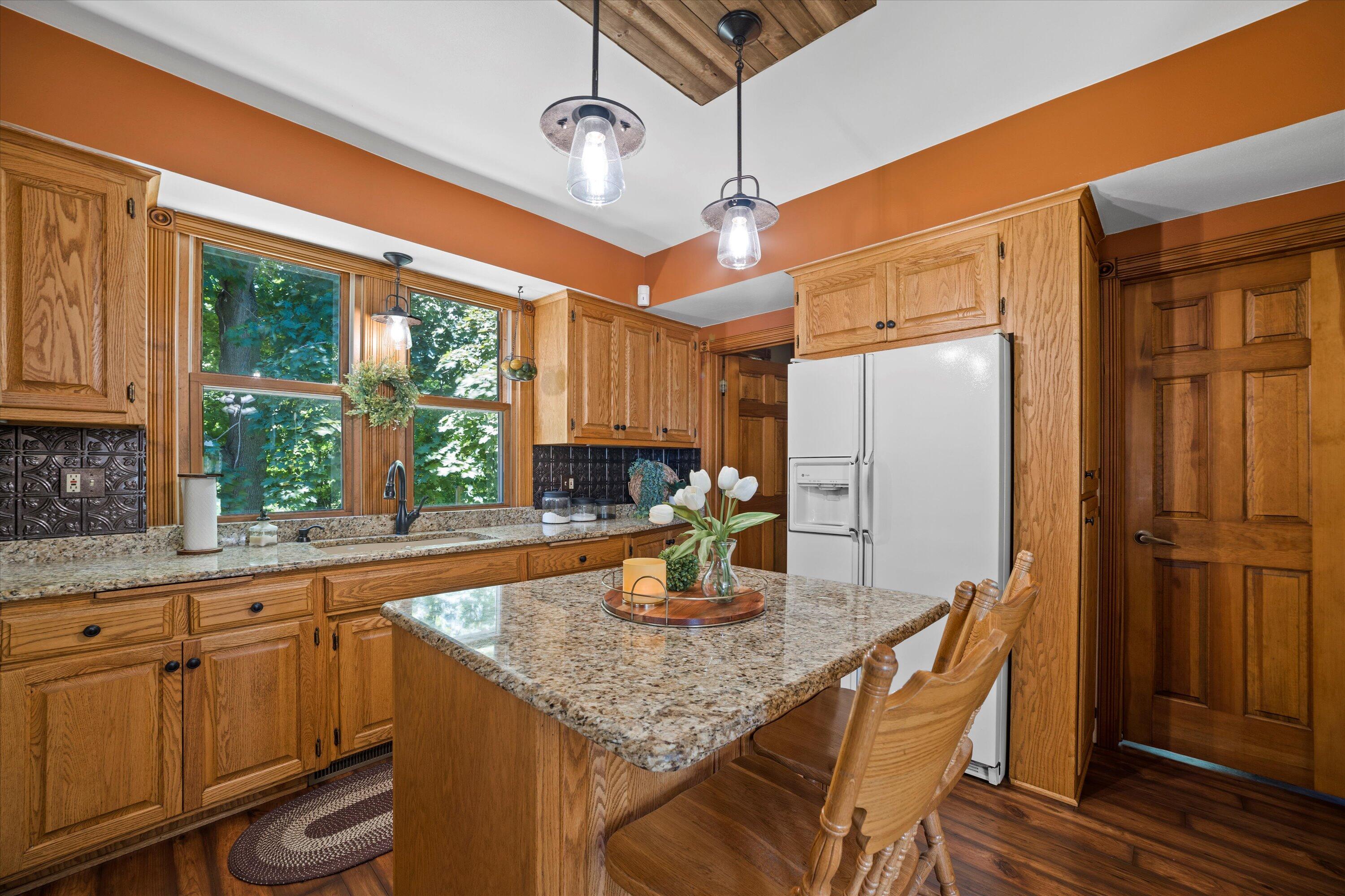 Kitchen with oak cabinetry, granite island, and large windows overlooking leafy trees.