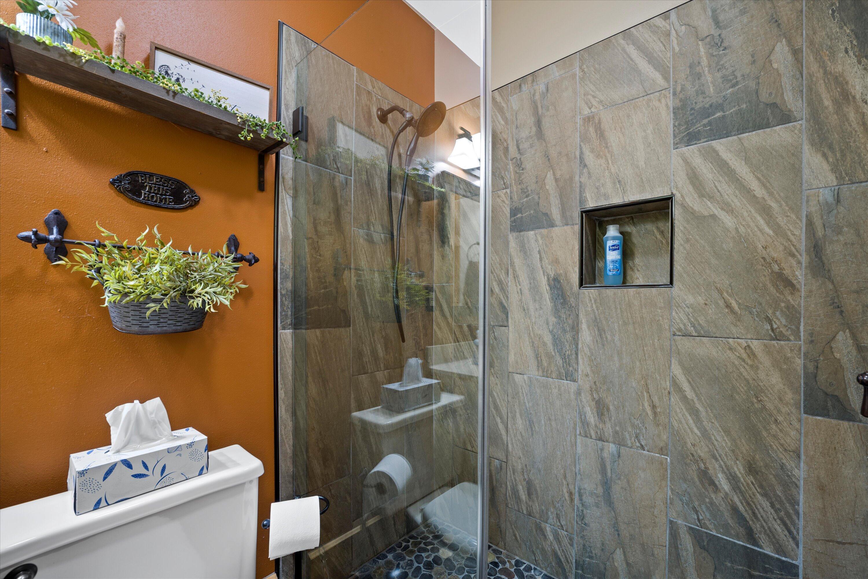 Bathroom with a glass-enclosed tiled shower, pebble floor, and orange accent wall.