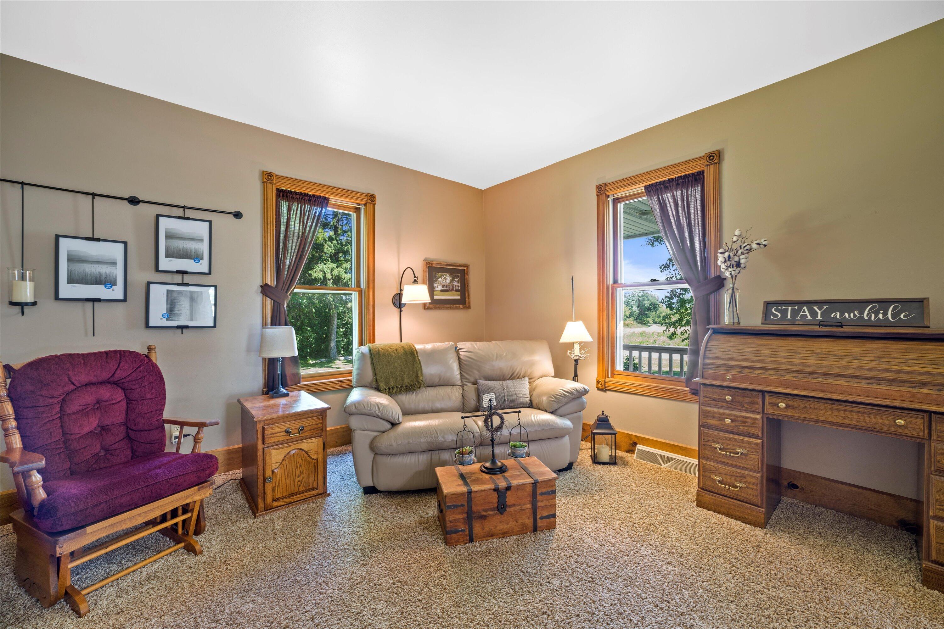 Living room with a cream sofa, purple rocking chair, and two large windows overlooking trees.