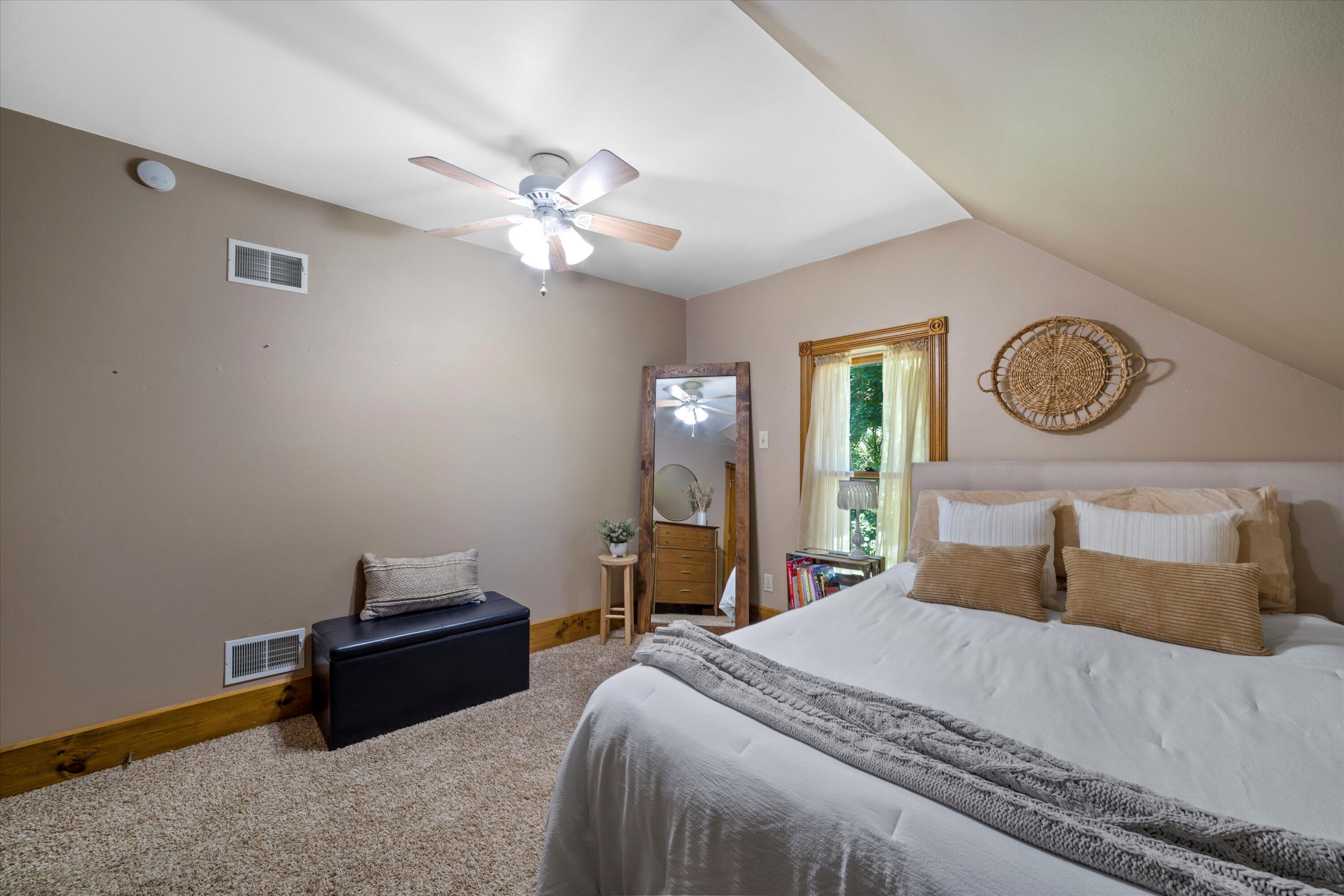 Furnished bedroom with a large bed beneath a vaulted ceiling and ceiling fan.