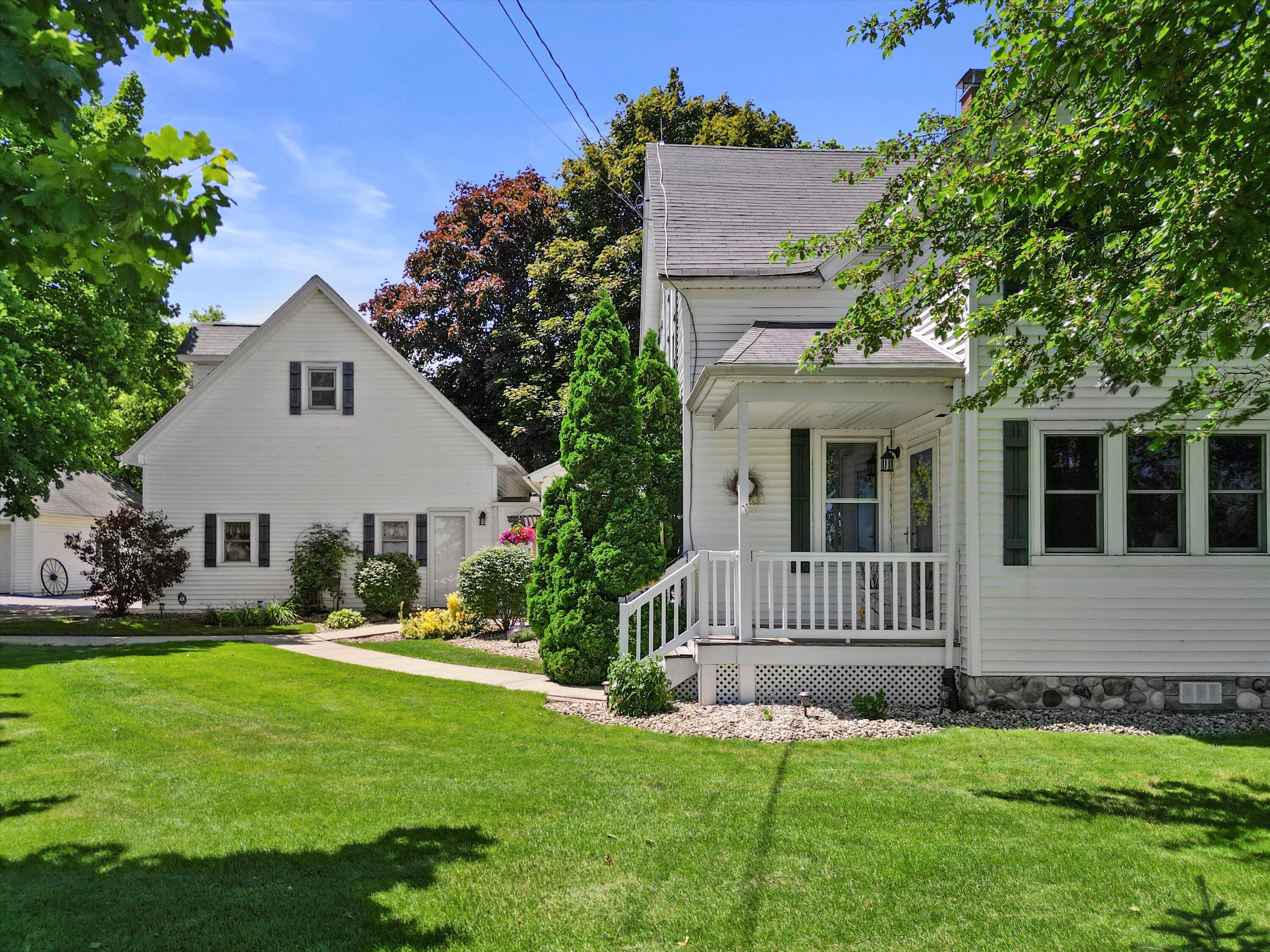 White-sided home with a covered porch, landscaped shrubs, and a broad green lawn.