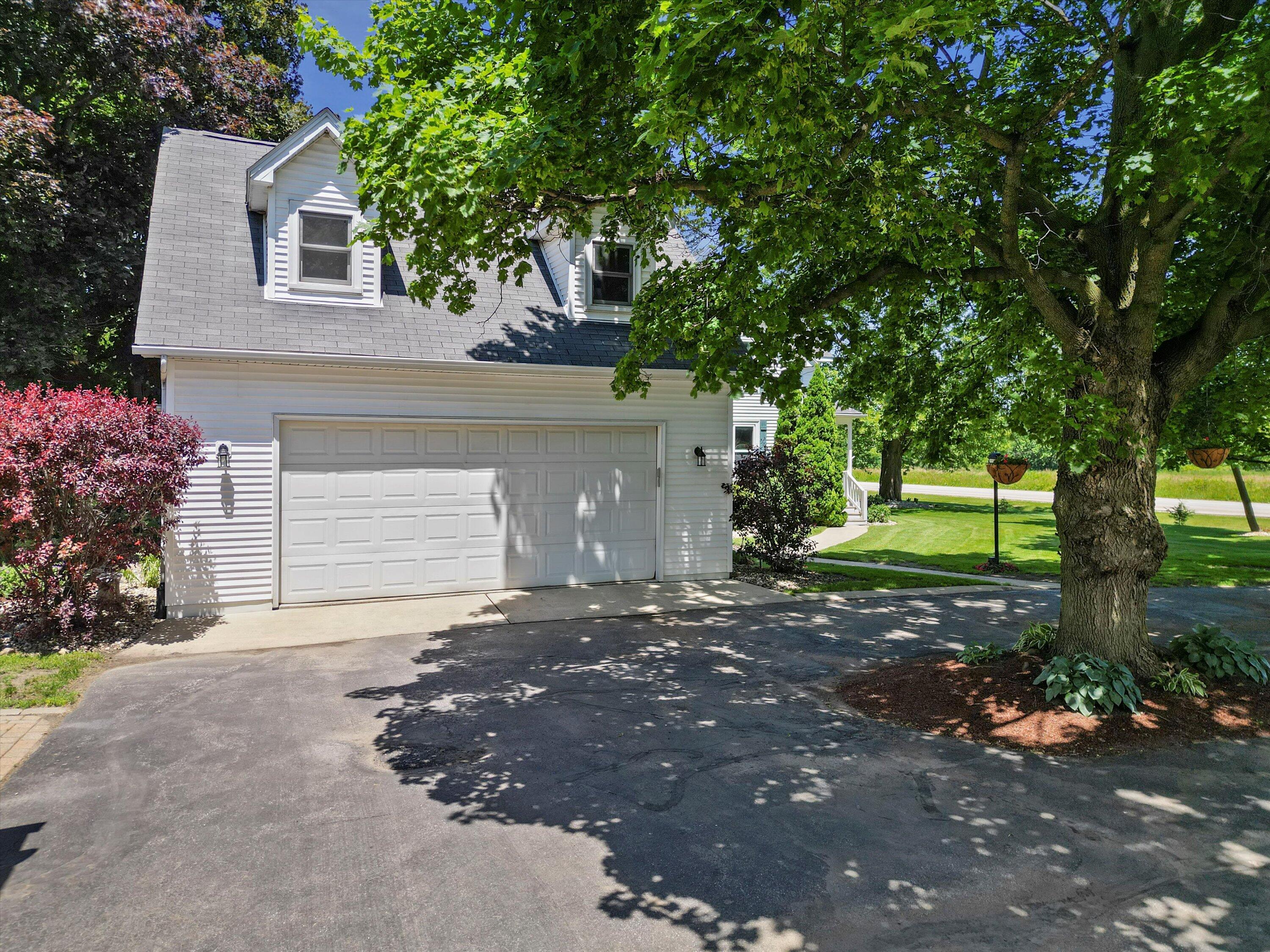 White two-story house with a double garage and driveway beneath a large shade tree.