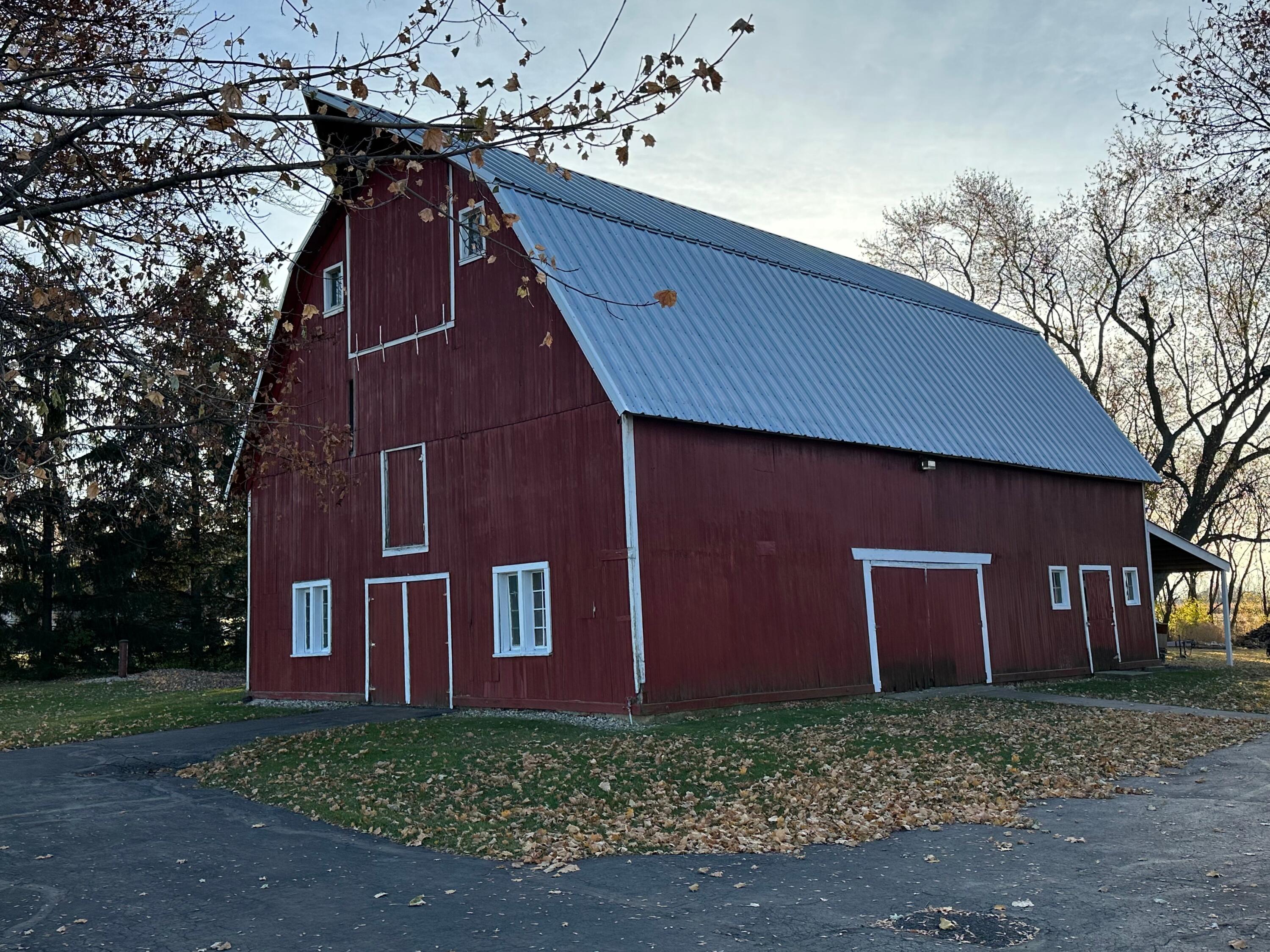 Red barn with a blue metal roof and white-trimmed doors, surrounded by autumn trees.