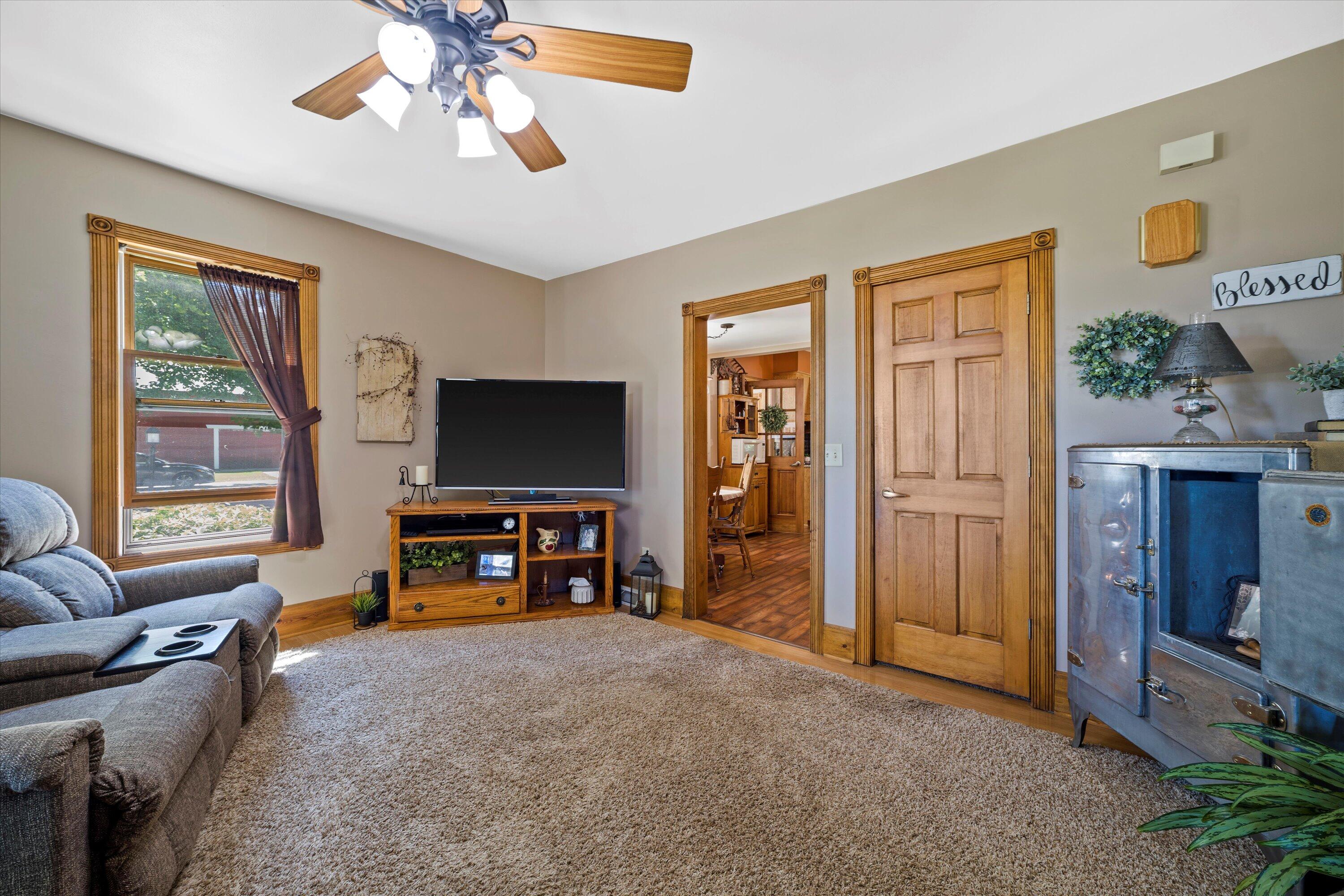 Living room with gray recliners, a television, carpeted floor, and wood-trimmed doorway to the dining area.