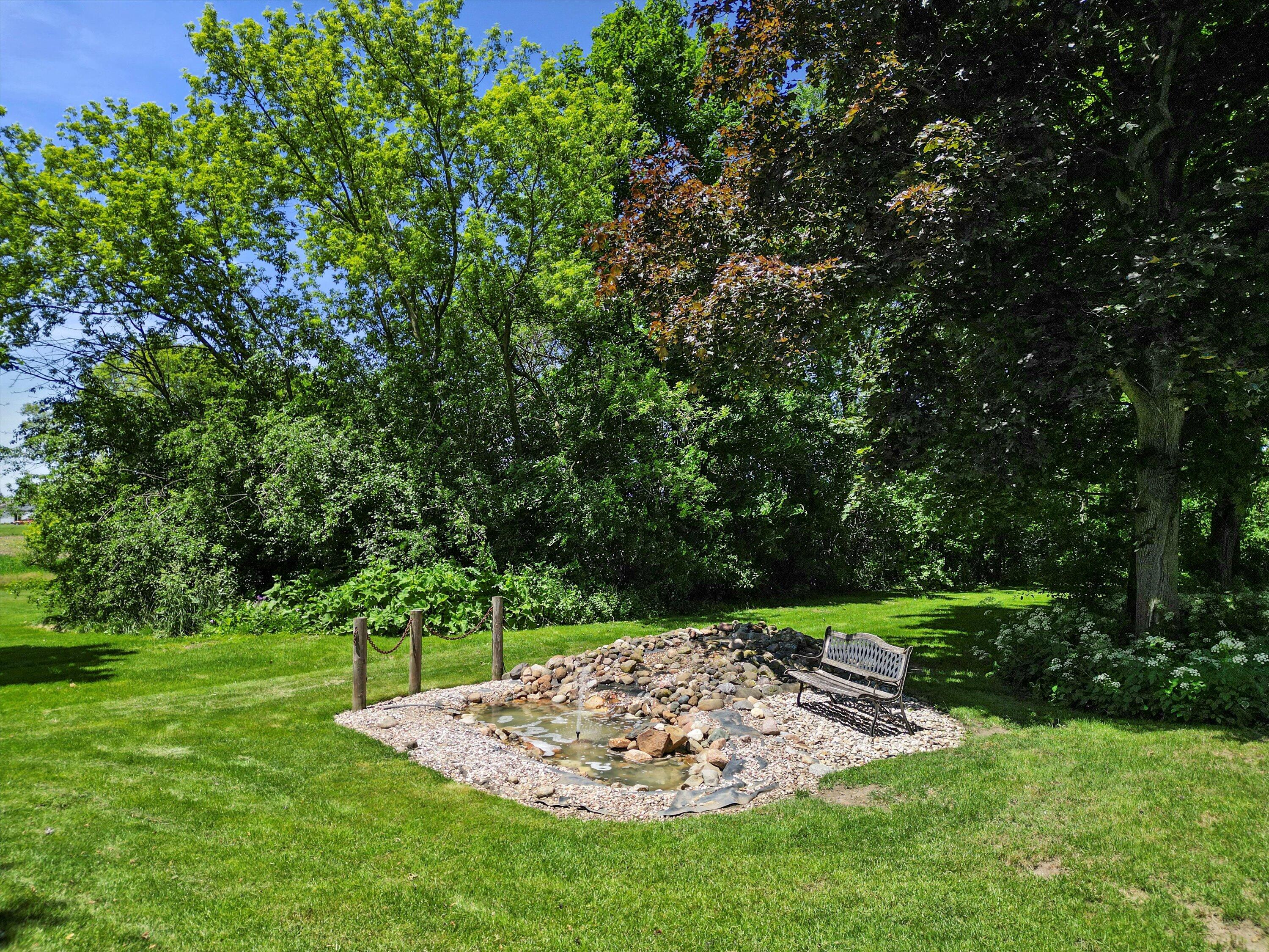 Landscaped backyard with a rock-lined pond and bench beneath mature trees.