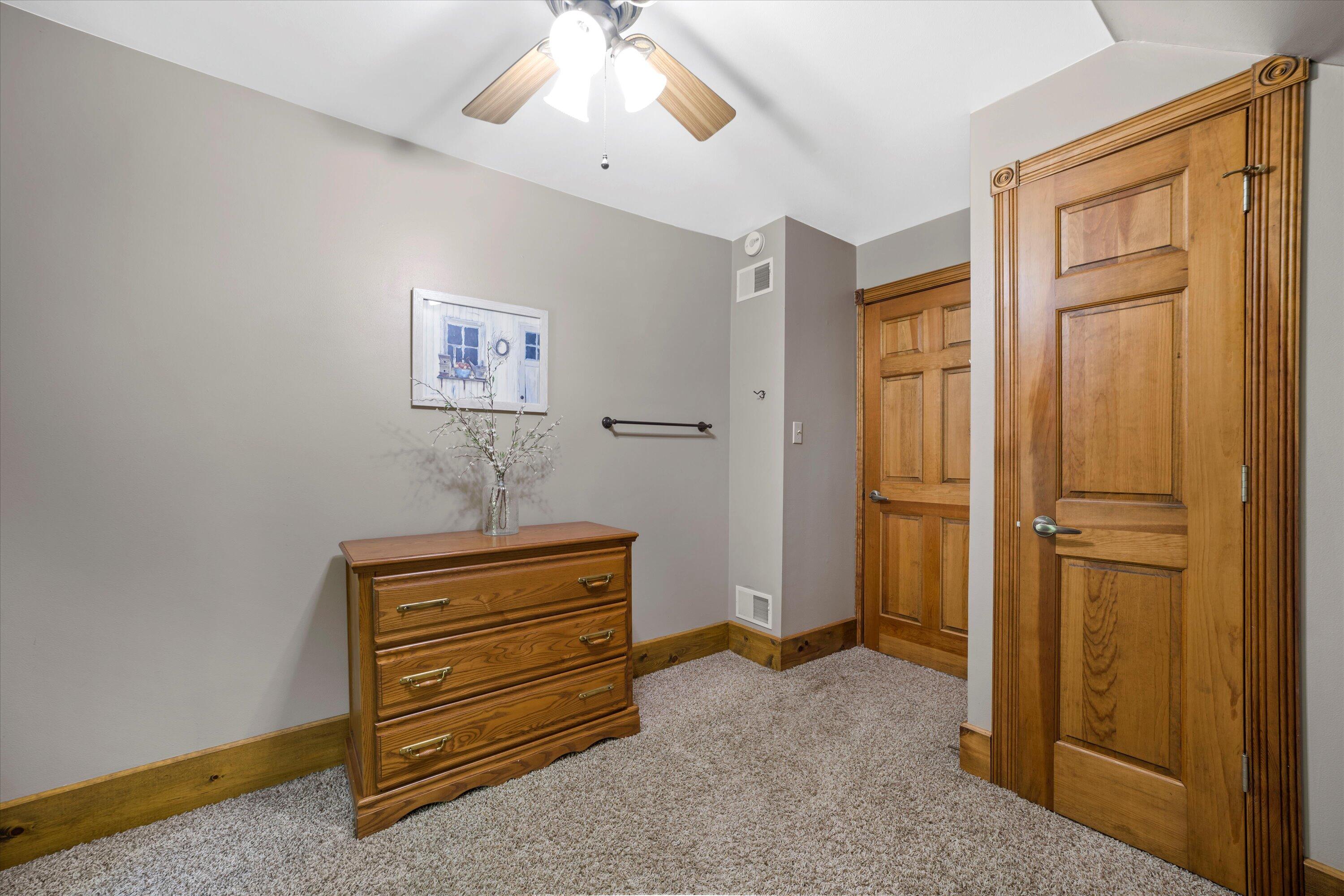 Bedroom with a wooden dresser, paneled doors, beige carpet, and a ceiling fan.