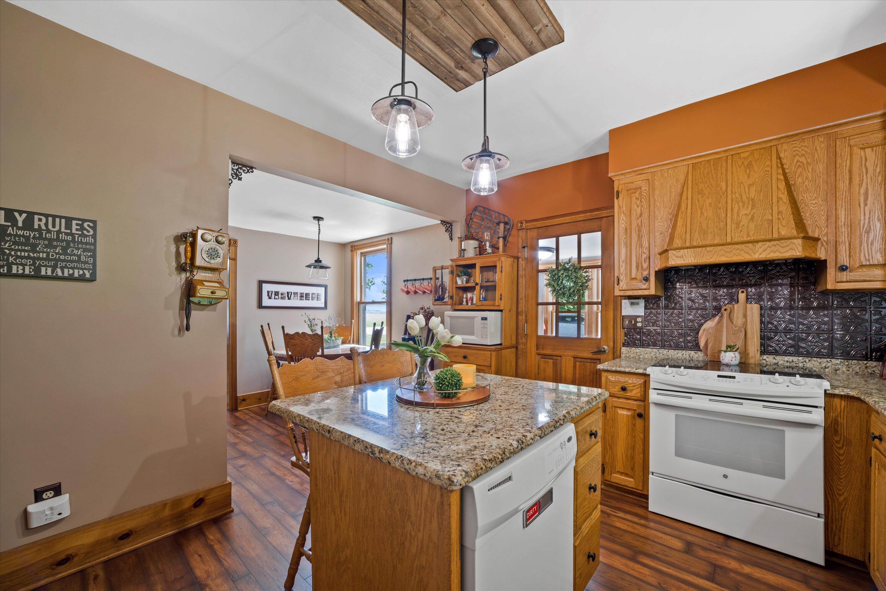 Kitchen with granite island, ornate dark tile backsplash, and adjoining dining area.