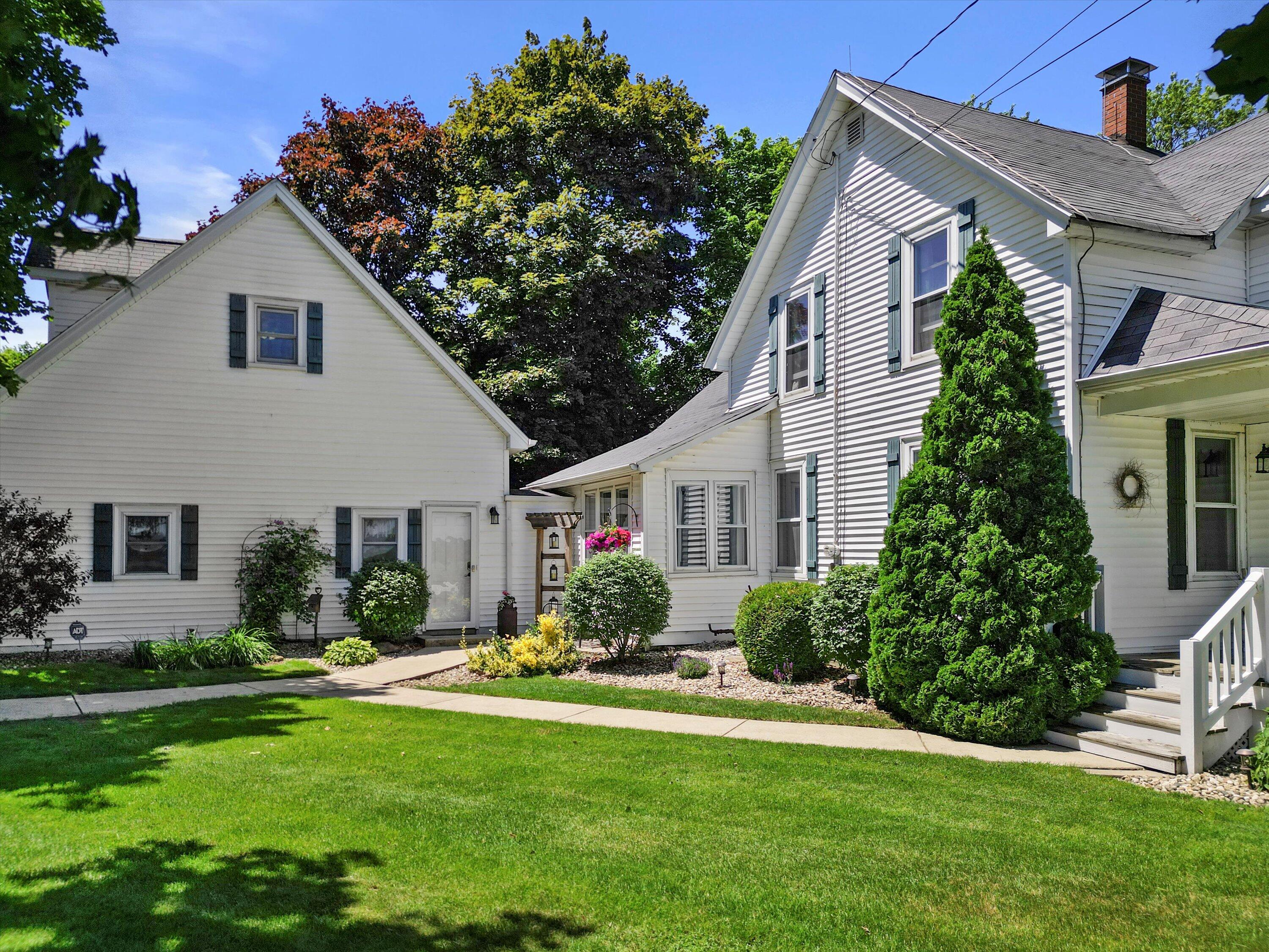 White house with dark shutters, landscaped shrubs, and a broad green front lawn.