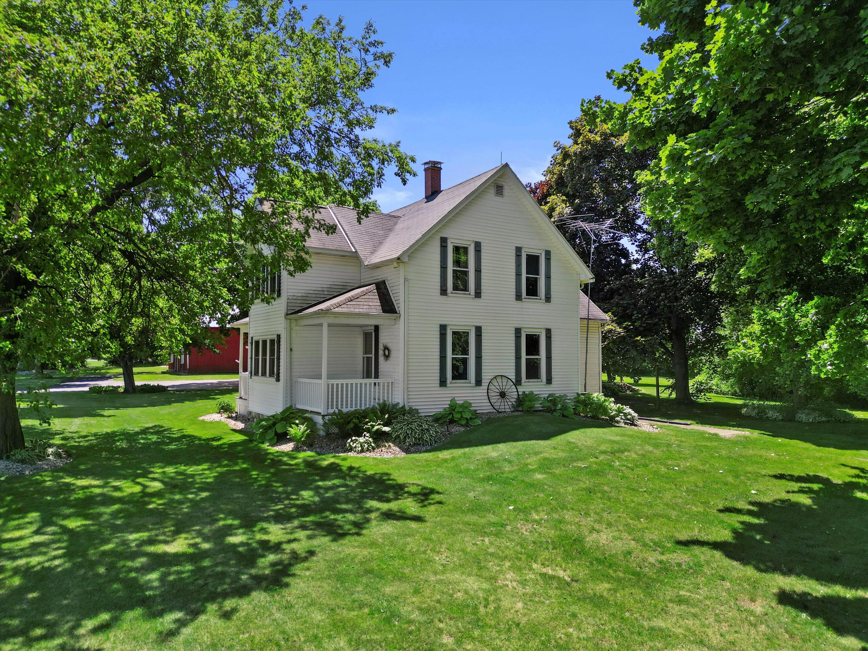White two-story house with dark shutters and a covered porch, framed by mature trees and a broad lawn.