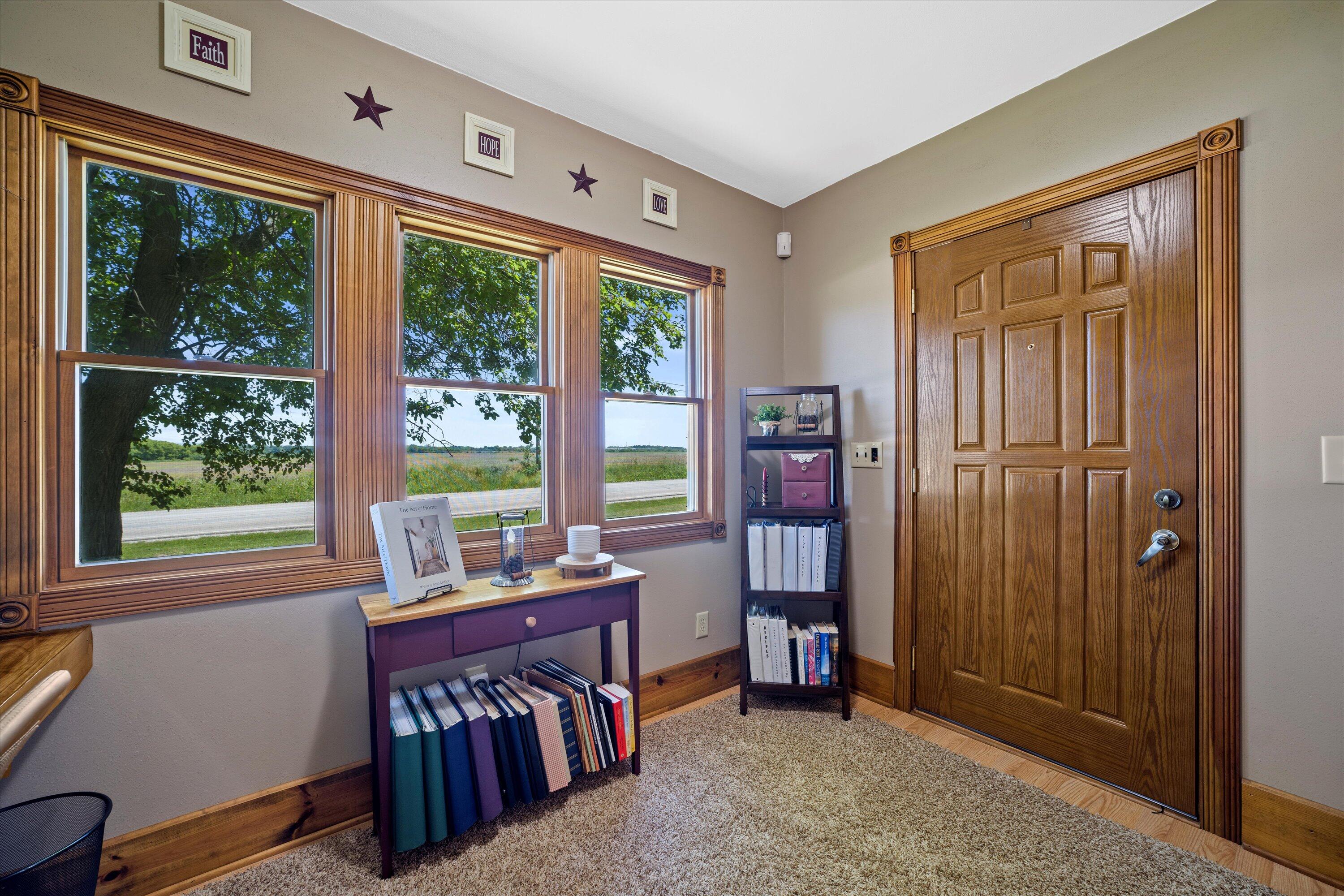 Home entryway with a paneled wooden door, three windows overlooking open fields, and a book-filled console table.