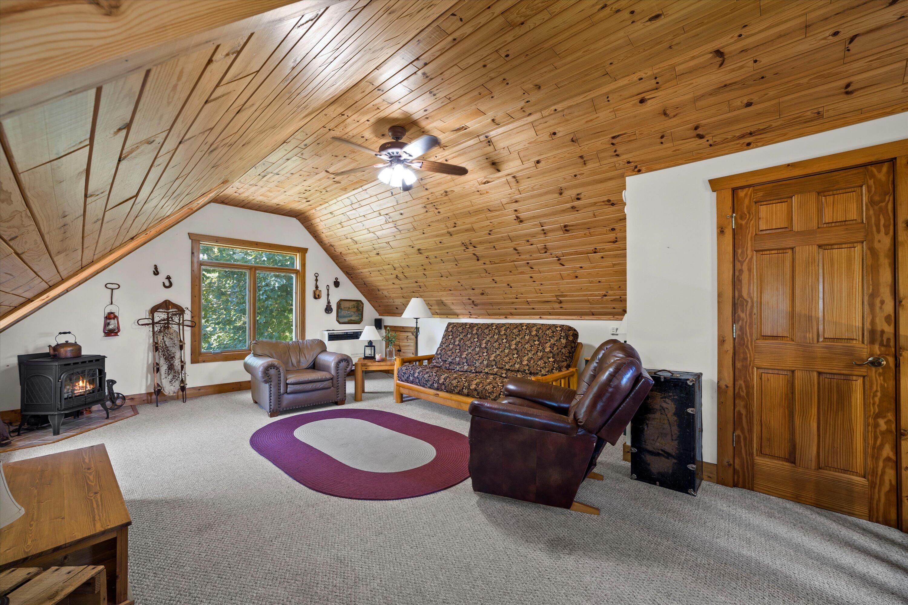 Furnished living room with a vaulted wood-plank ceiling, leather seating, and a wood-burning stove.