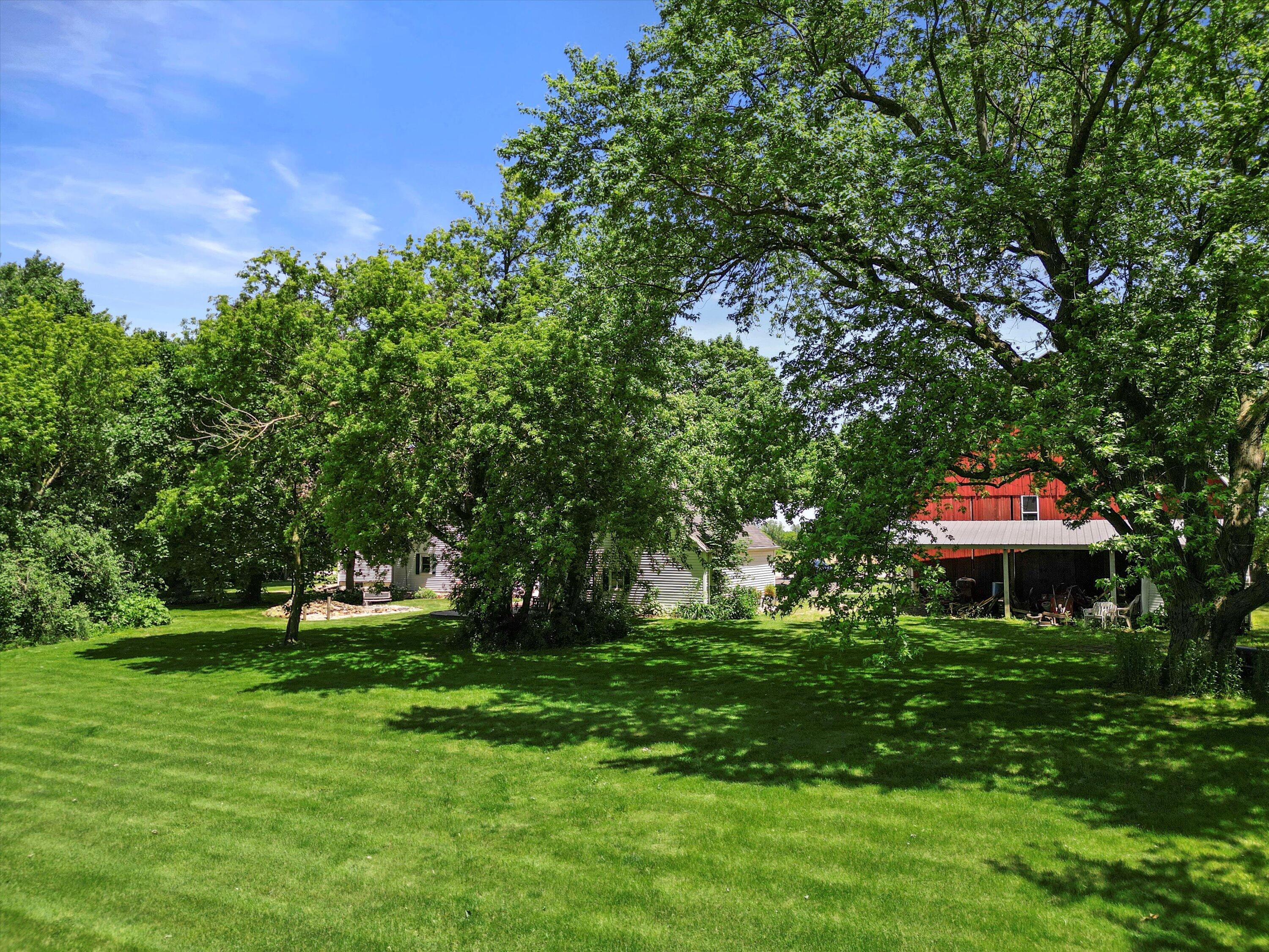 White-sided house and red barn beyond a shady lawn and mature trees.