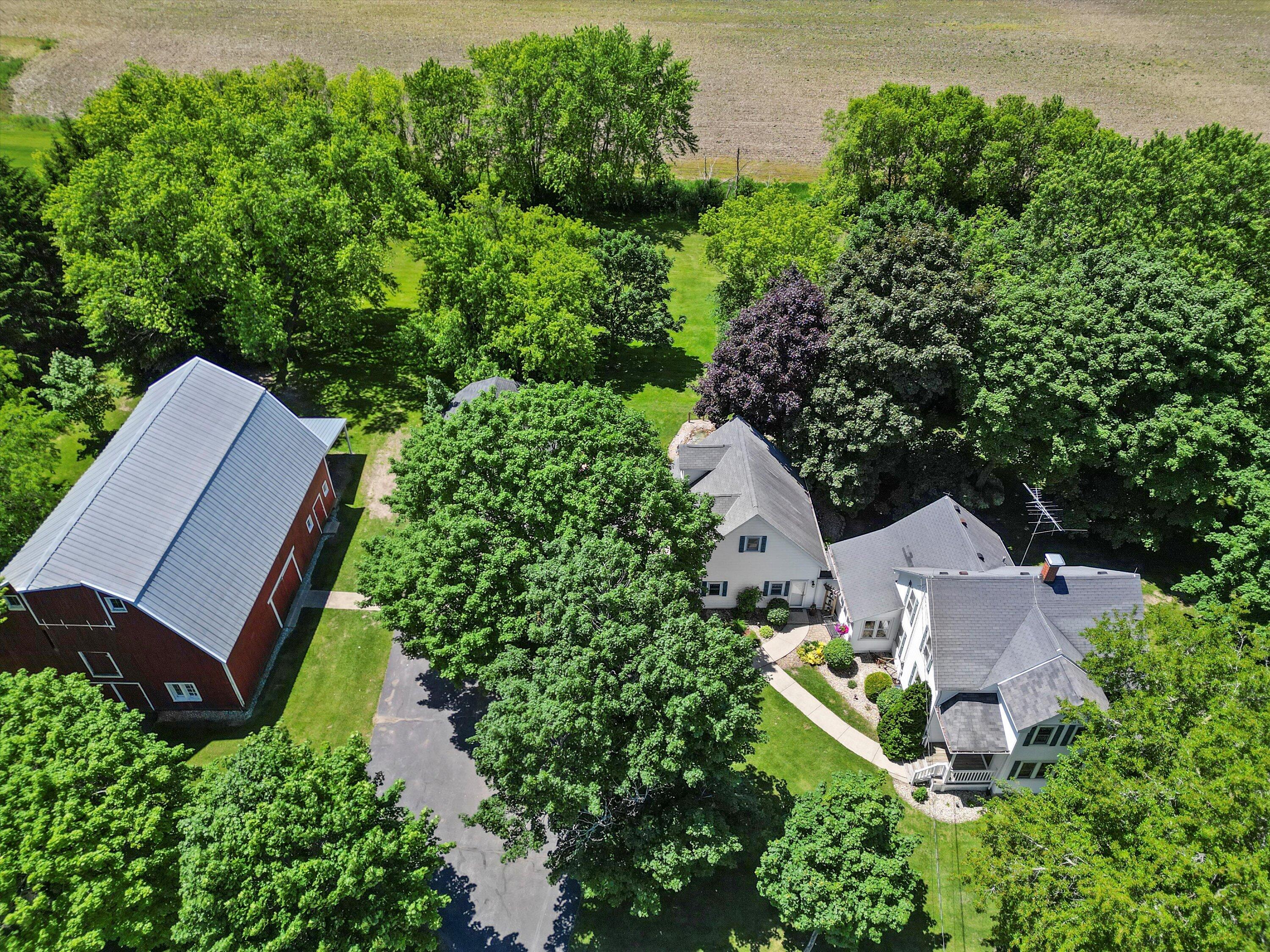 Aerial view of a white home and red barn surrounded by mature trees and lawn.